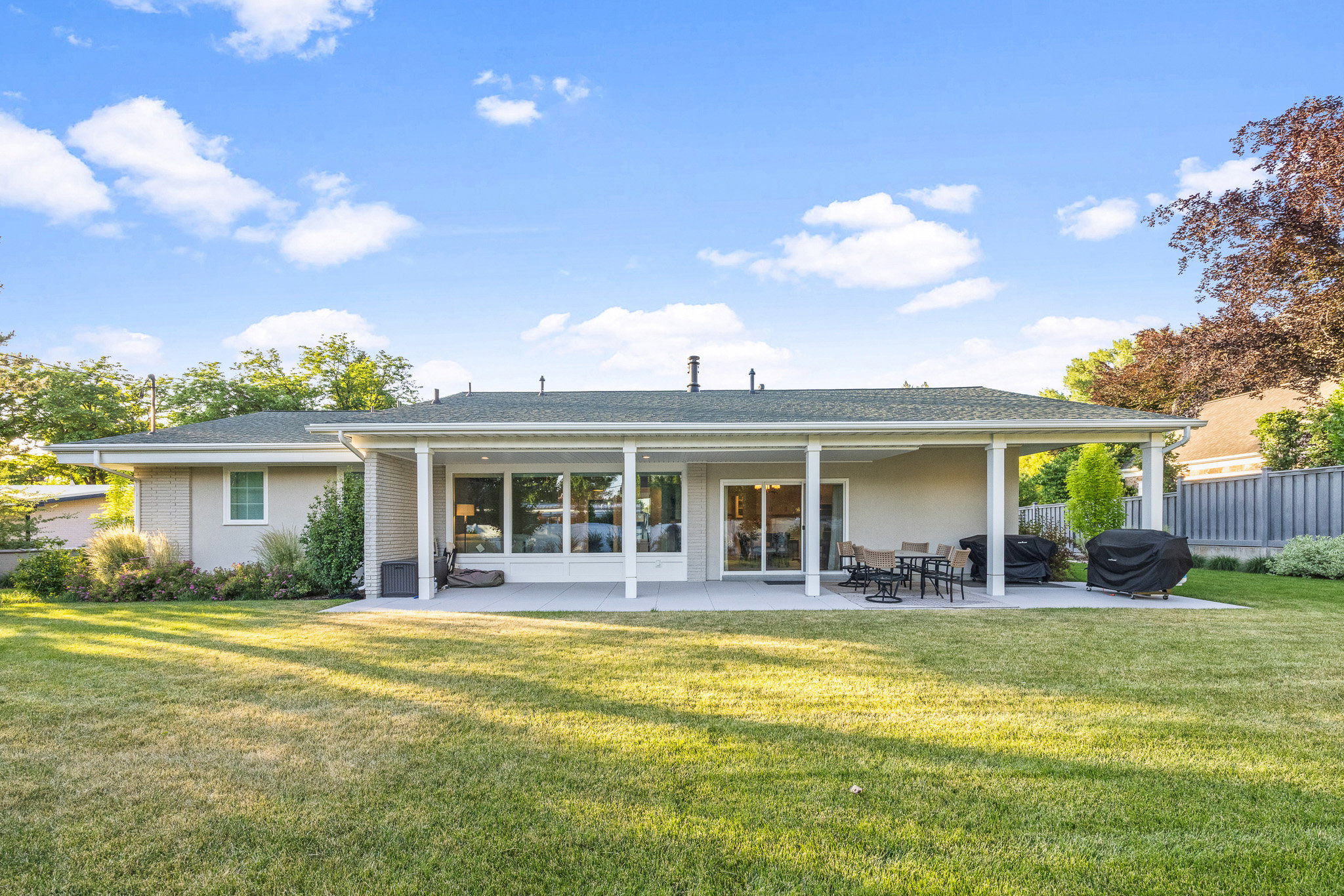 Expansive rear exterior featuring a covered patio, multiple large windows, and a sliding glass door
