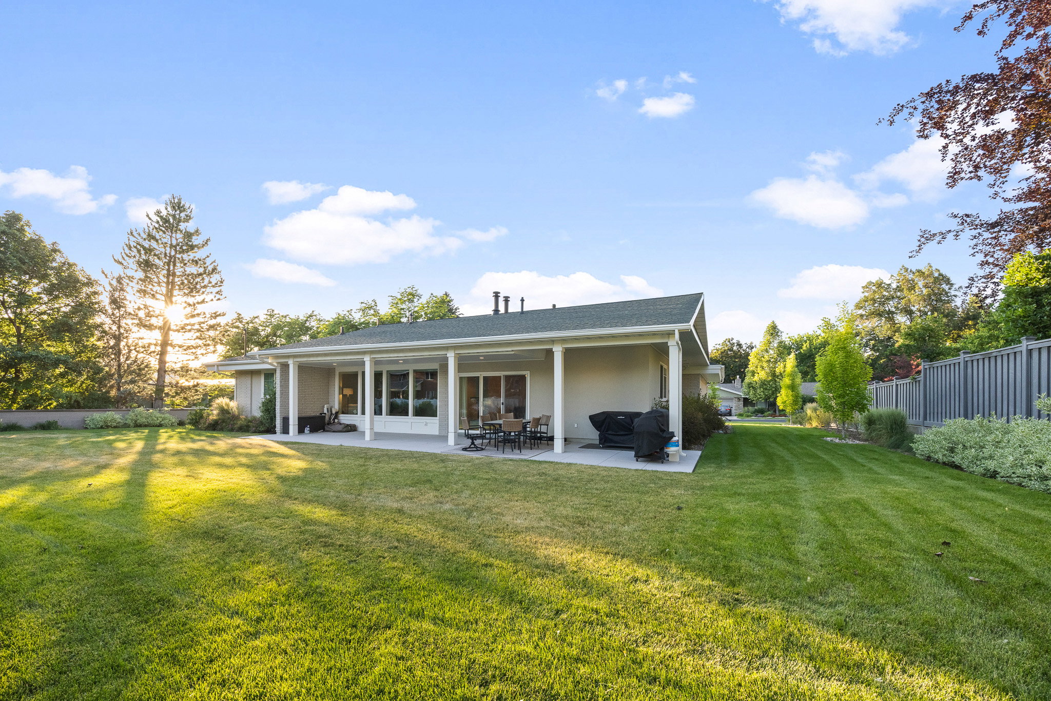 Expansive lawn with mature landscaping surrounds a covered patio