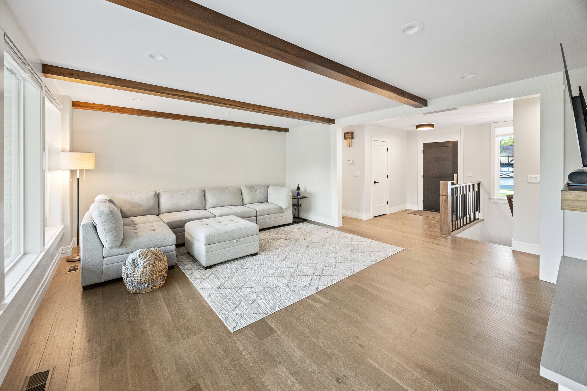 Spacious living area featuring light wood-finish flooring, exposed ceiling beams, recessed lighting, and large windows