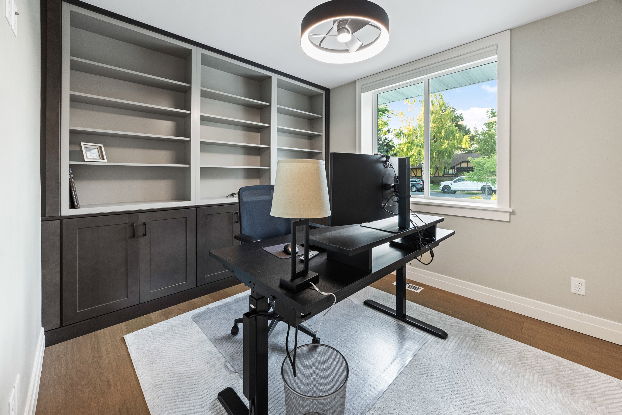 Room featuring custom built-in shelving with lower cabinetry, wood-finish flooring, and a large window