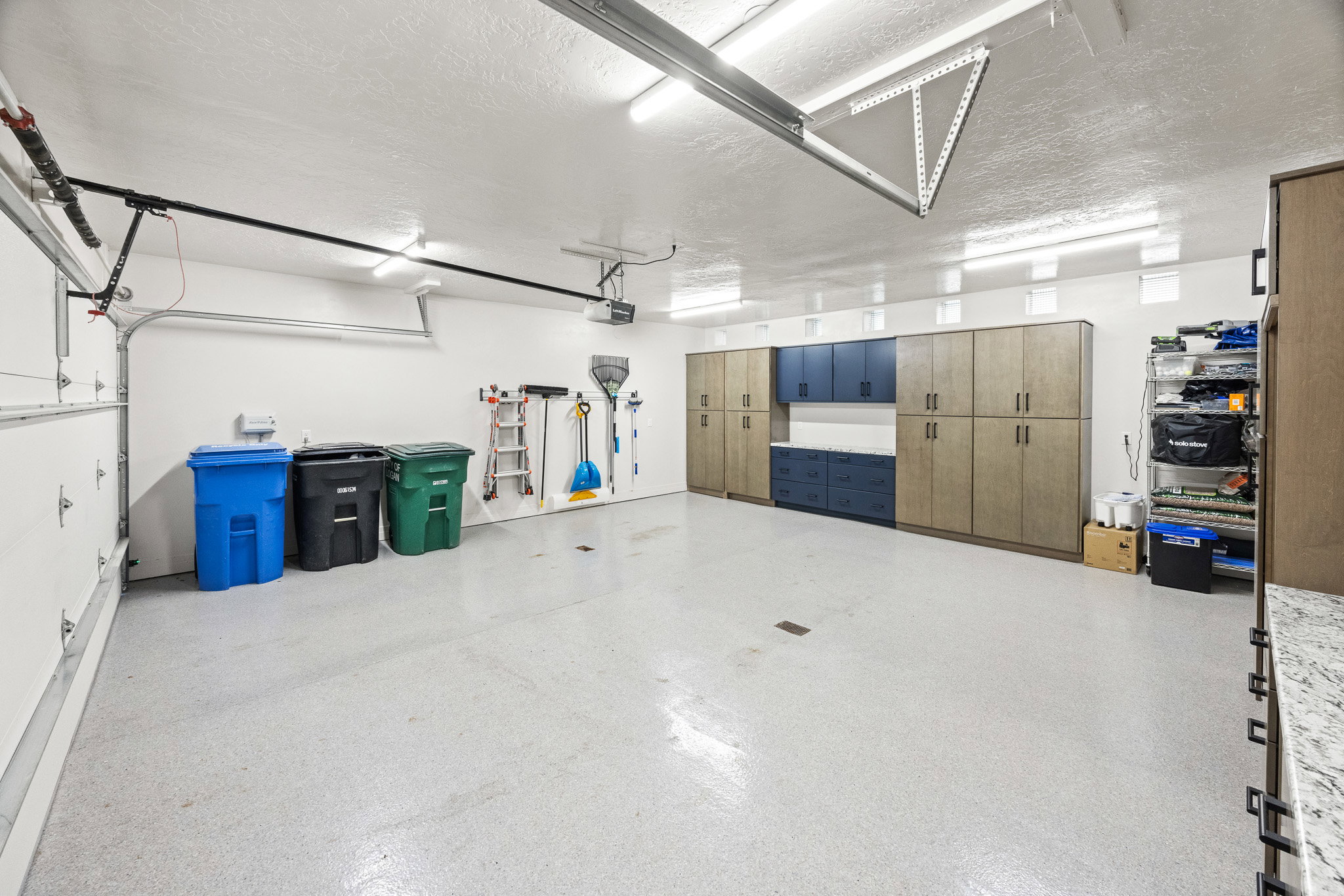 Spacious garage featuring an epoxy-coated floor, integrated cabinetry, ample overhead lighting, and an automatic garage door opener