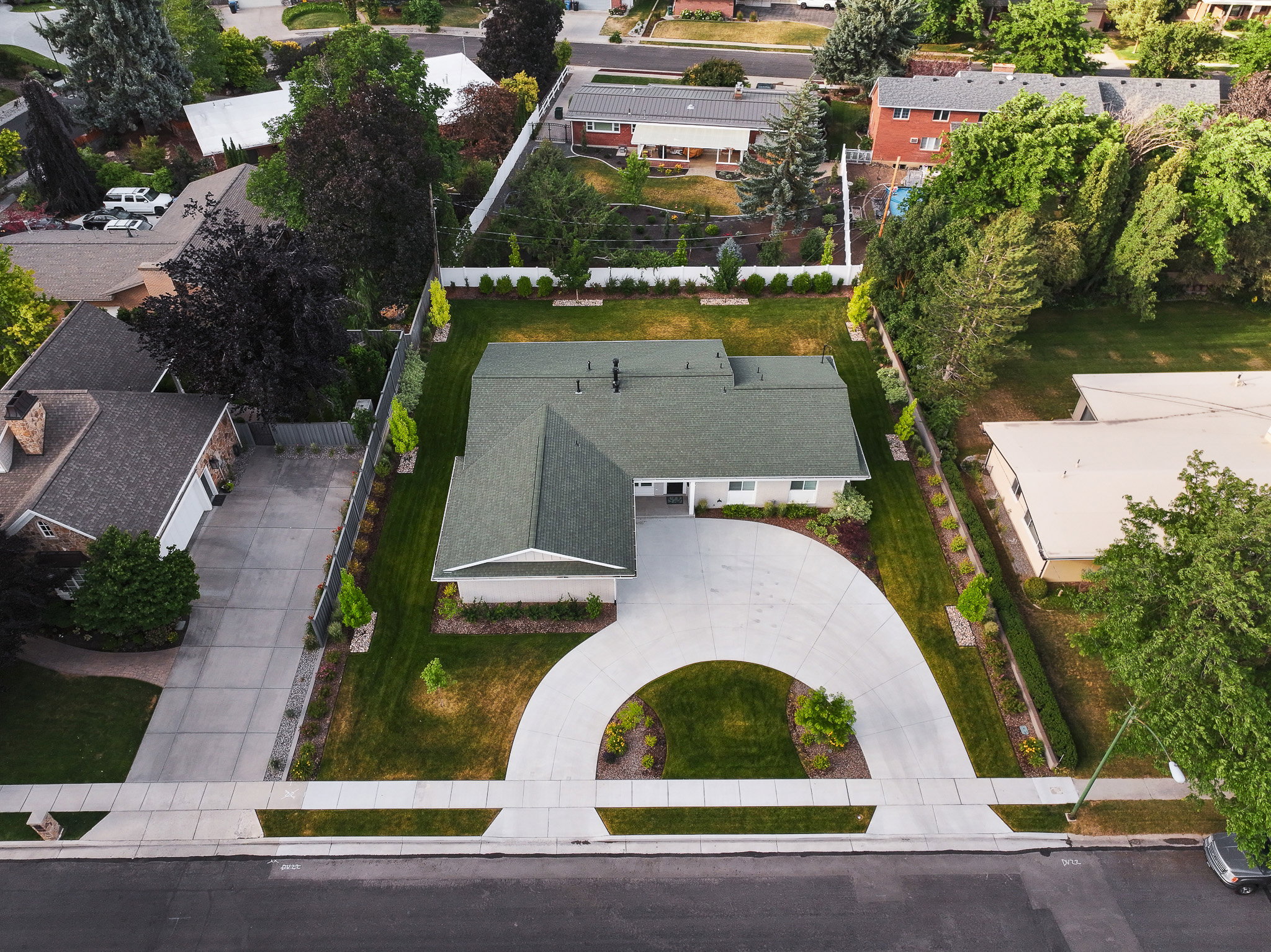 Ranch-style residence featuring a prominent circular driveway, a dark green asphalt shingle roof, and a beige exterior