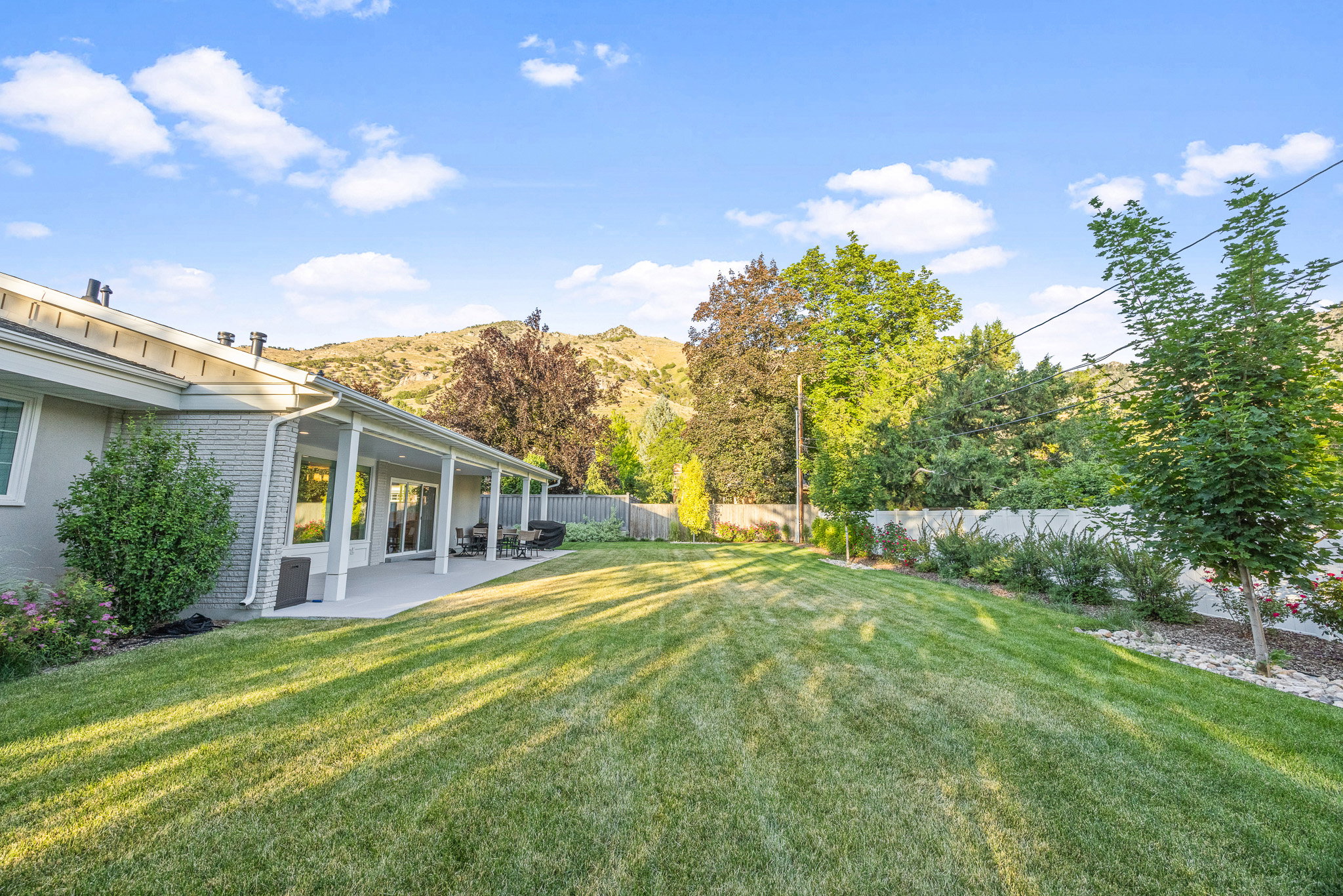Expansive backyard featuring a manicured lawn, a full-length covered patio, and a backdrop of mountainous terrain