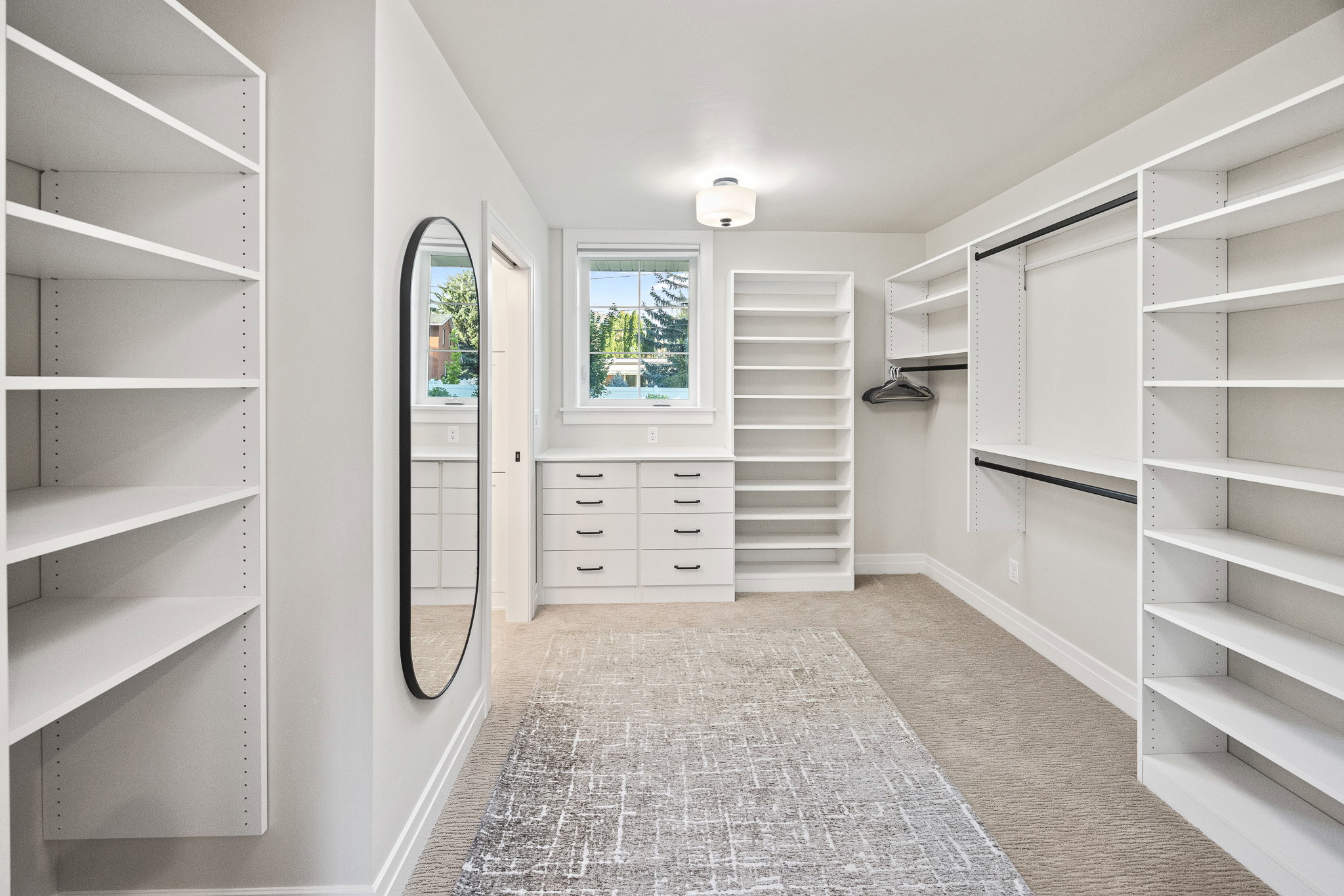 Spacious walk-in closet featuring extensive built-in shelving, integrated drawer storage, dual hanging rods, and a large oval mirror