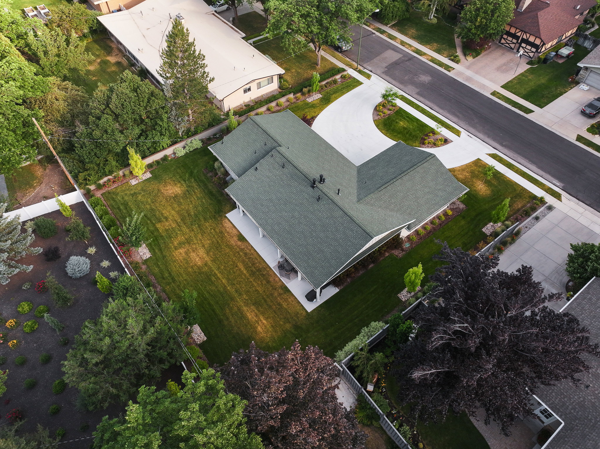 Expansive property featuring a dark green shingled roof, a paved driveway, a large lawn, and mature trees