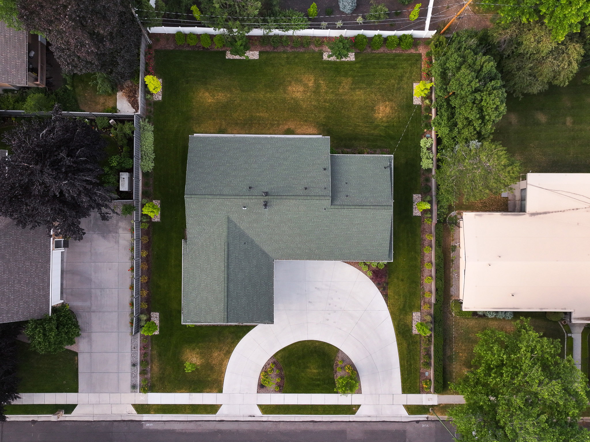 L-shaped residential structure with a green shingle roof, a curved concrete driveway, and a front lawn bordered by landscaping
