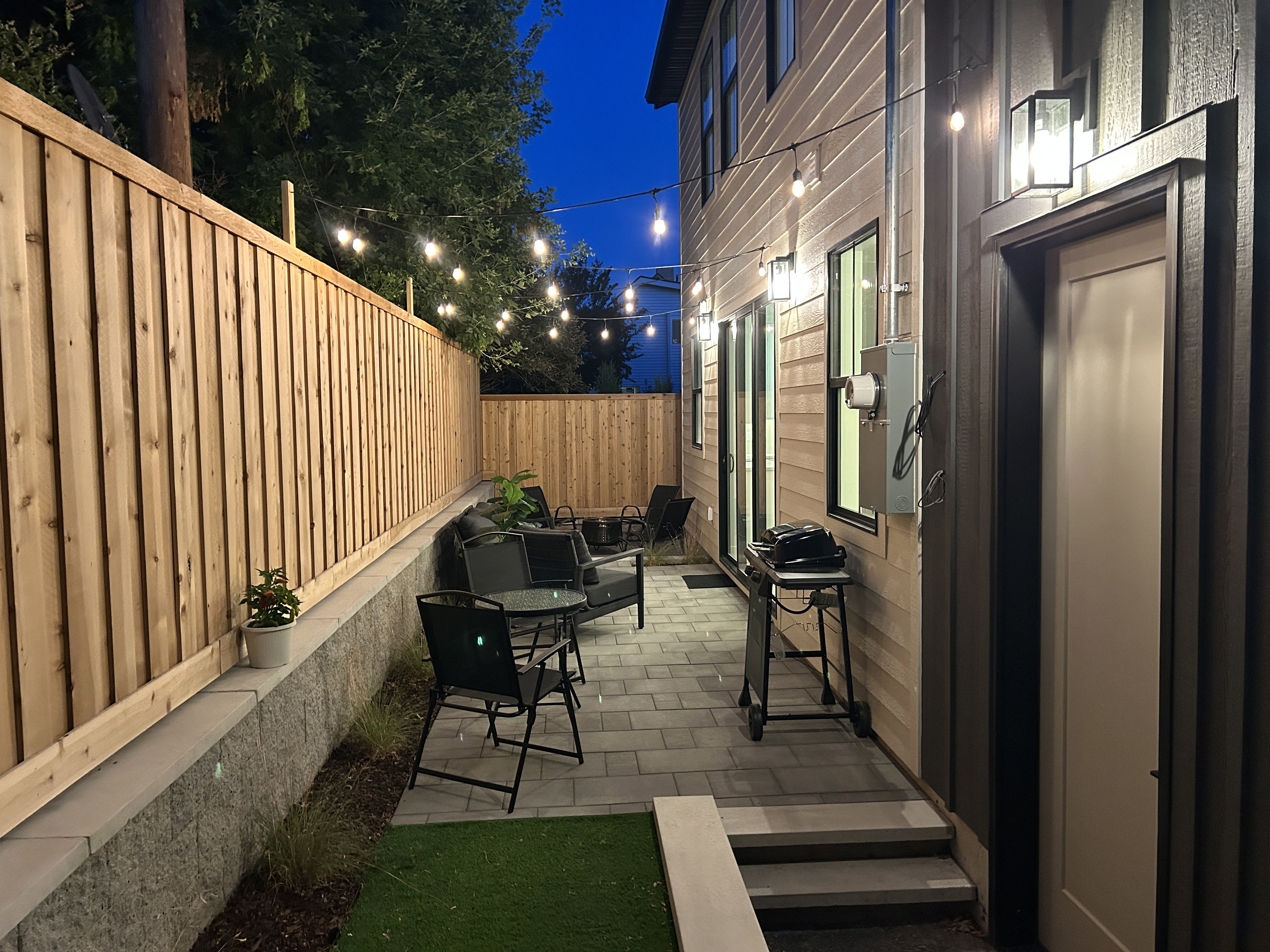 Outdoor patio area featuring string lighting, privacy fencing, and a paver stone surface