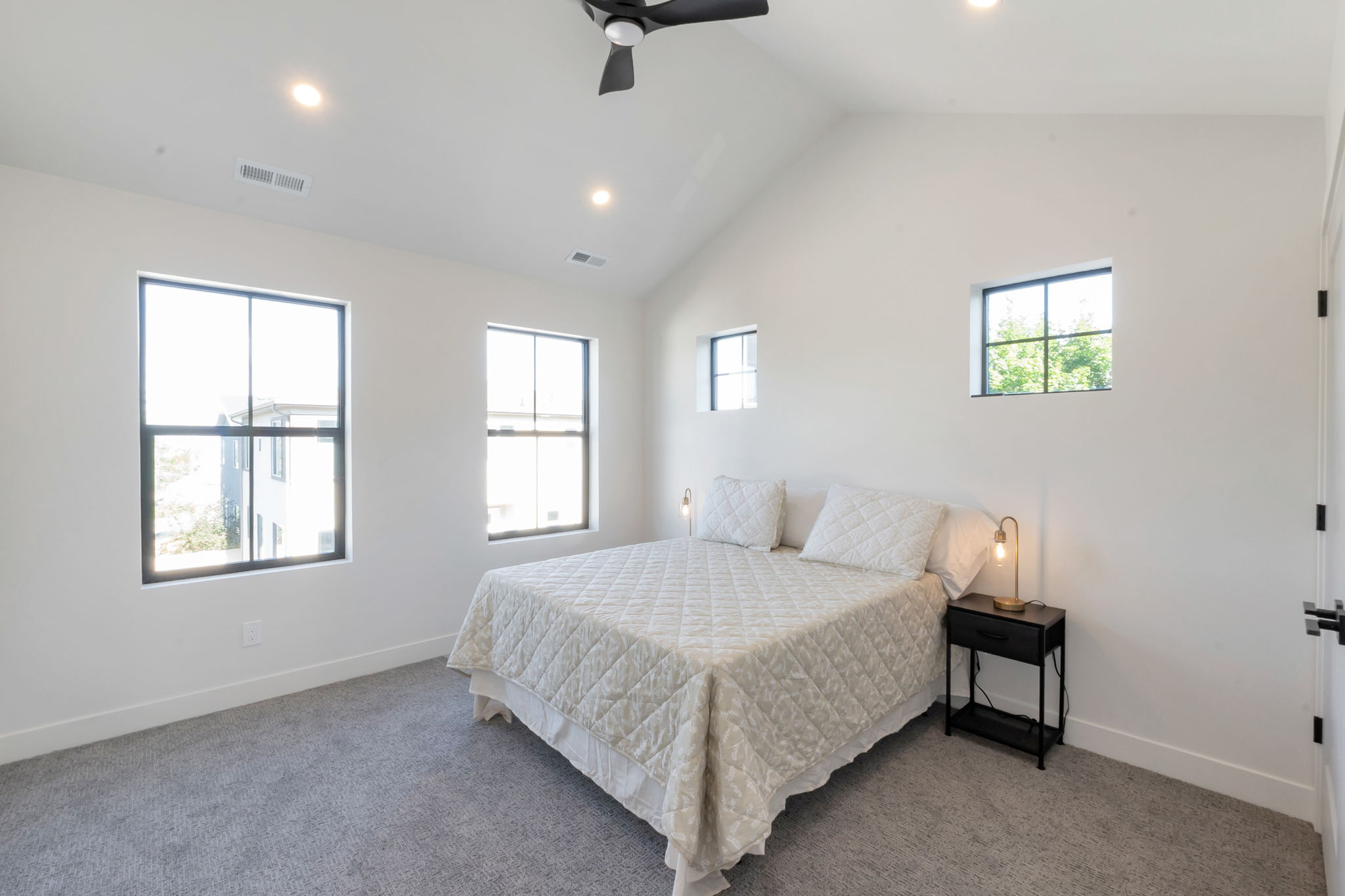 Vaulted ceiling bedroom featuring four black-framed windows, recessed lighting, and a ceiling fan