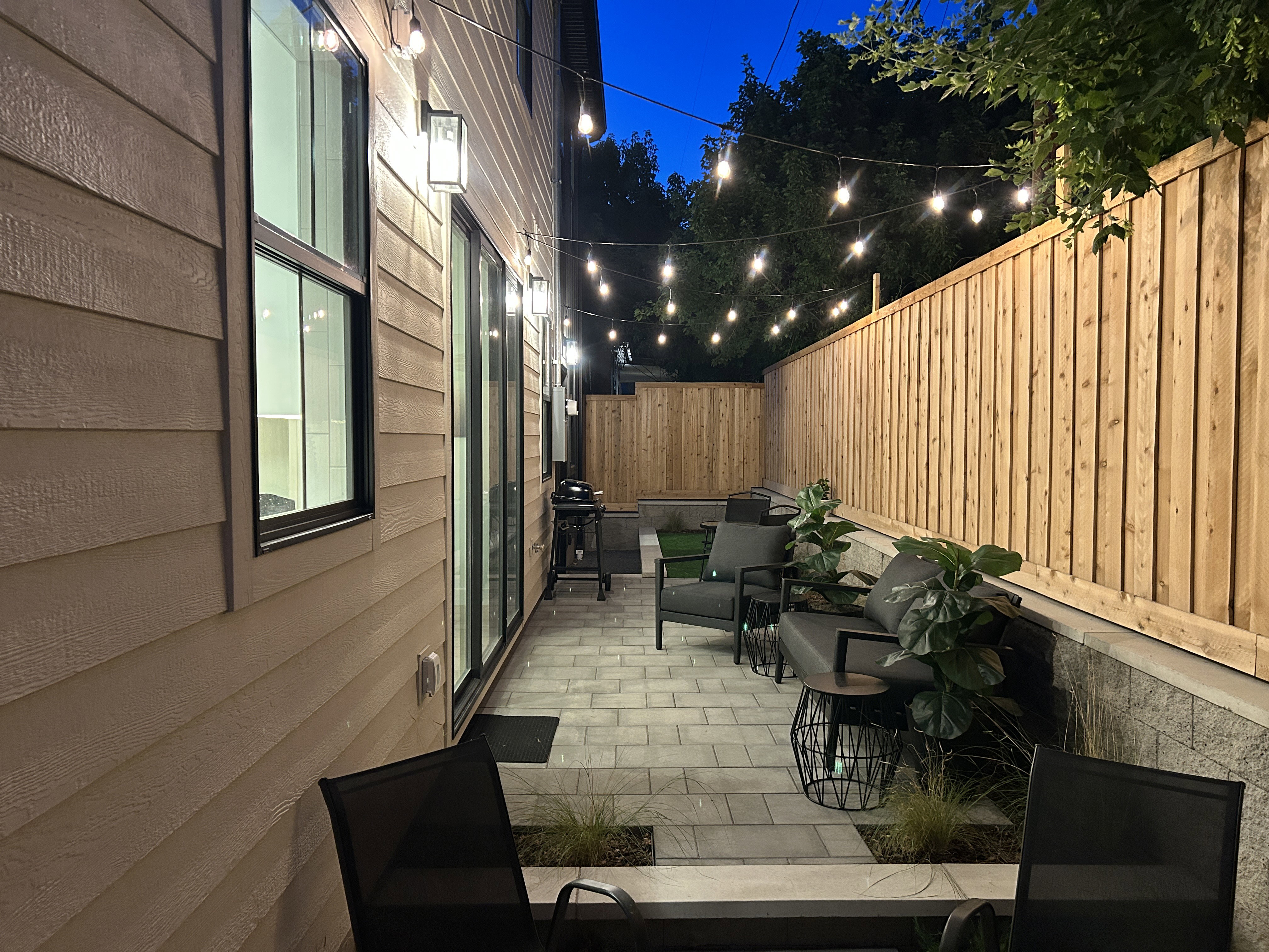 Private outdoor patio featuring paver flooring, a wood privacy fence, and string lighting