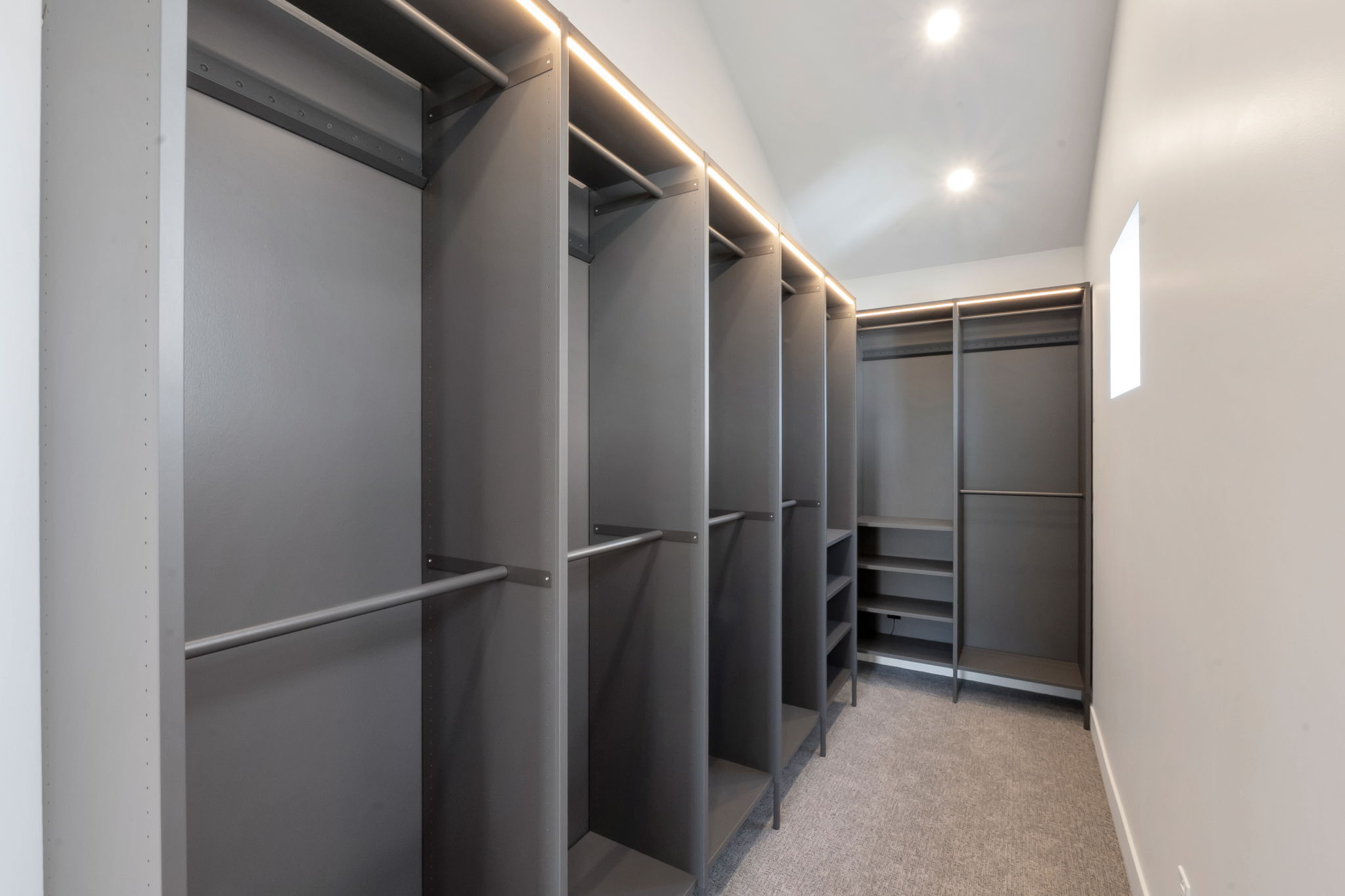 Custom closet system featuring multiple hanging rods, shelving, recessed lighting, and soft carpet flooring