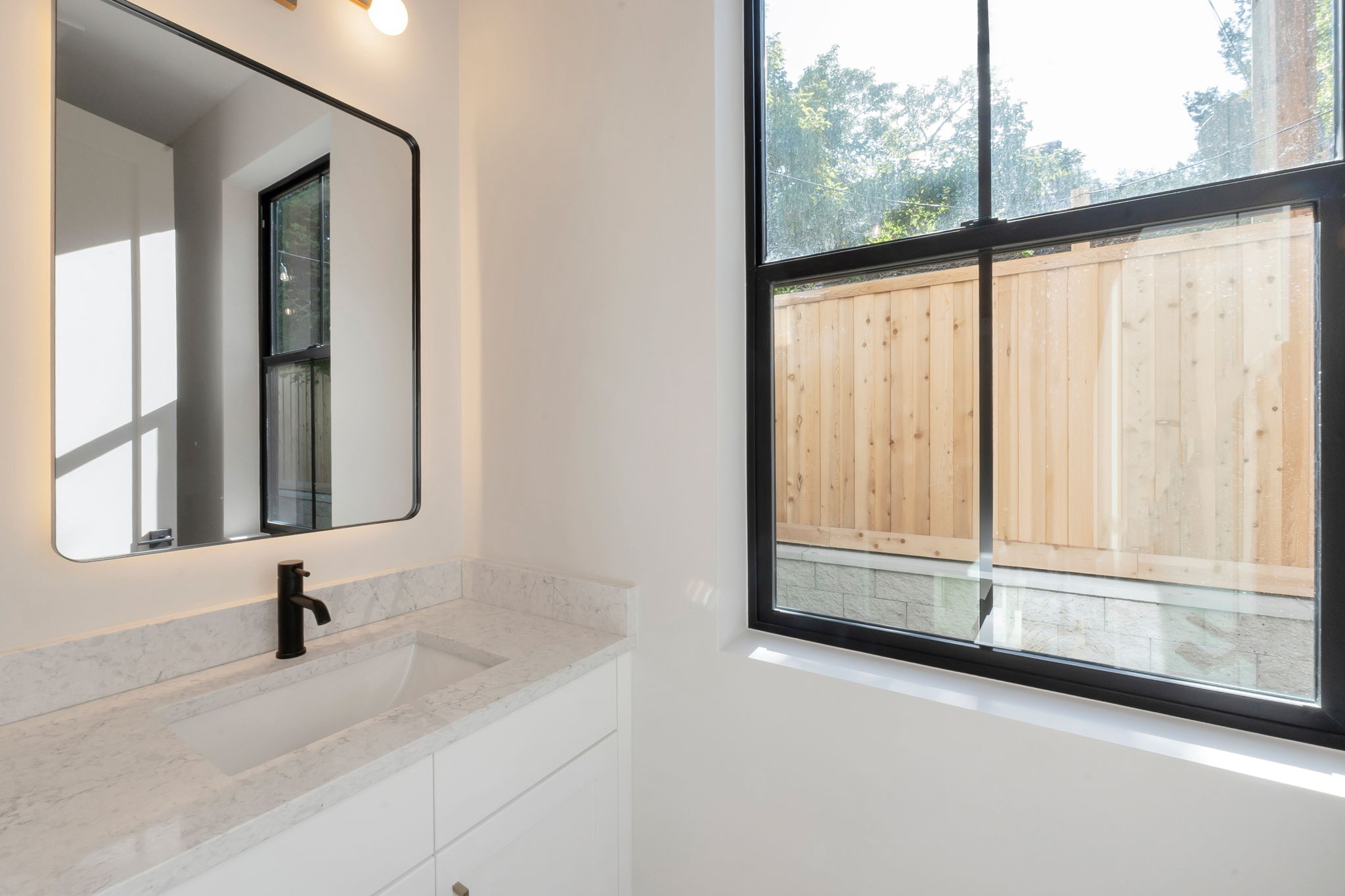 White vanity with a subtle veined countertop, undermount sink, and matte black faucet