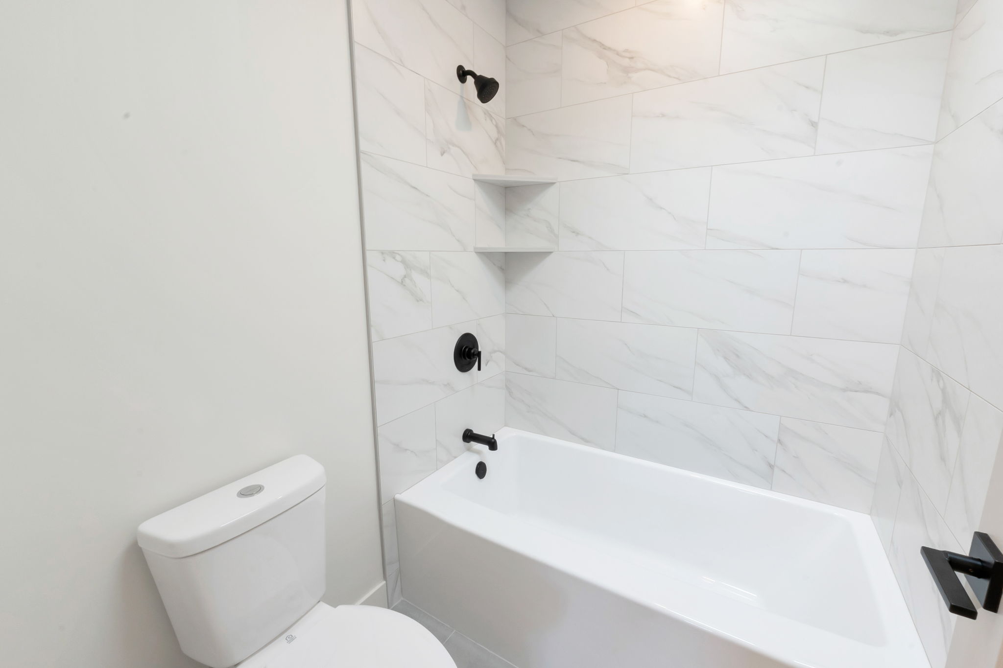 Bathroom featuring a white bathtub, white wall-mounted toilet, and large format marble-look tile surround