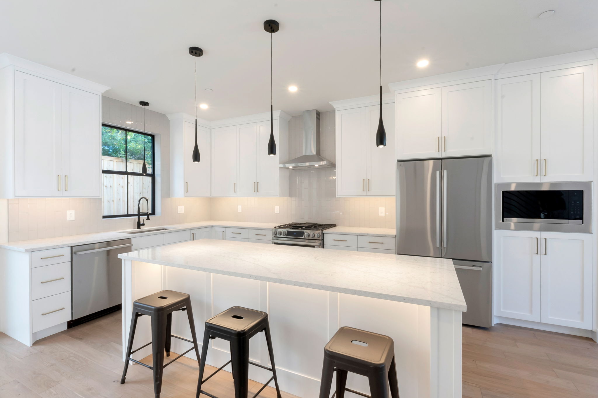 Kitchen featuring white shaker cabinetry, stainless steel appliances, light-toned countertops, pendant lighting, and wood-finish flooring