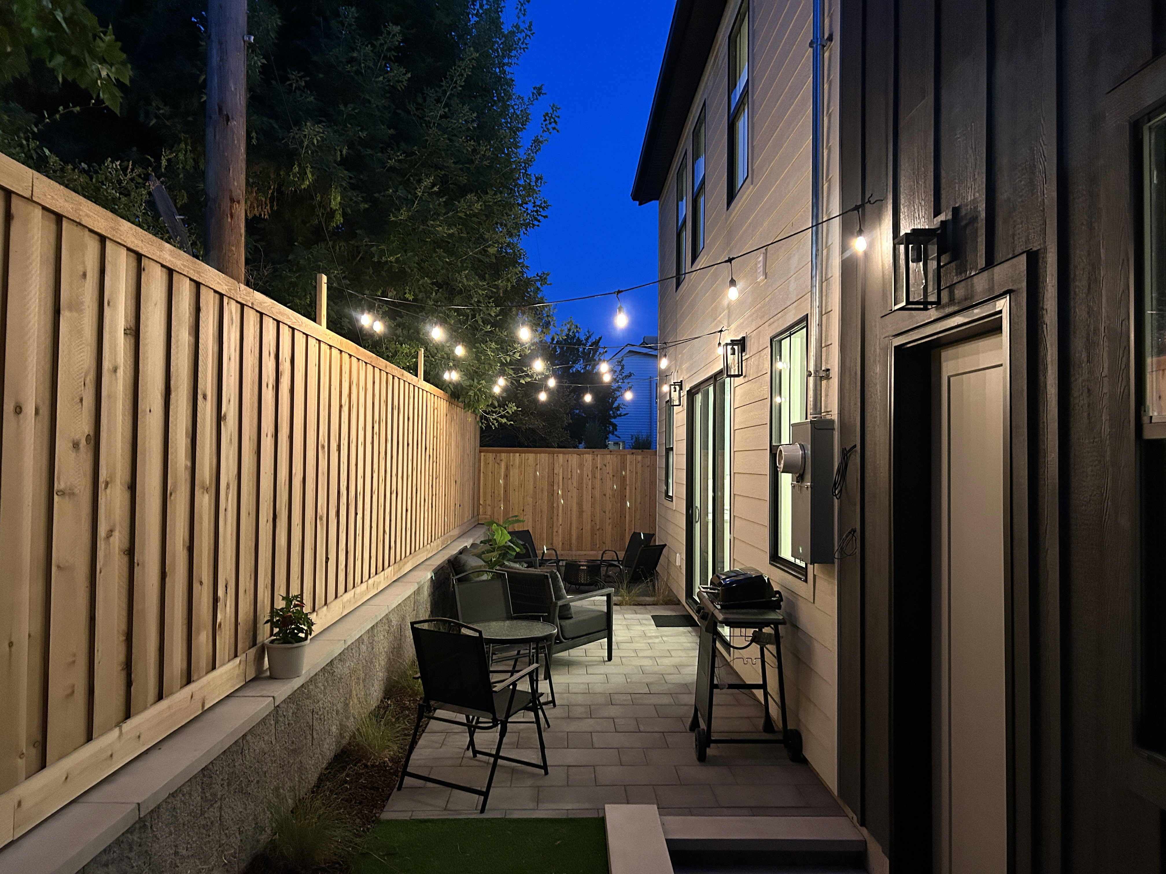Private patio space featuring paver flooring, a new wood privacy fence, and modern exterior wall lighting