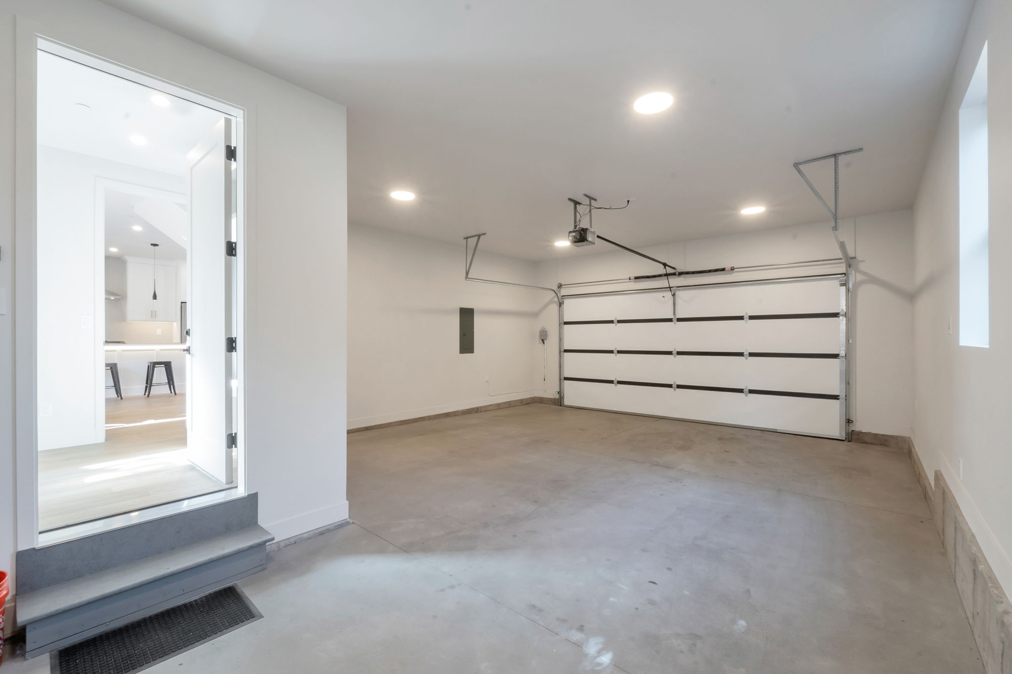 Attached garage featuring a white sectional door, concrete flooring, recessed lighting, and a window for natural light