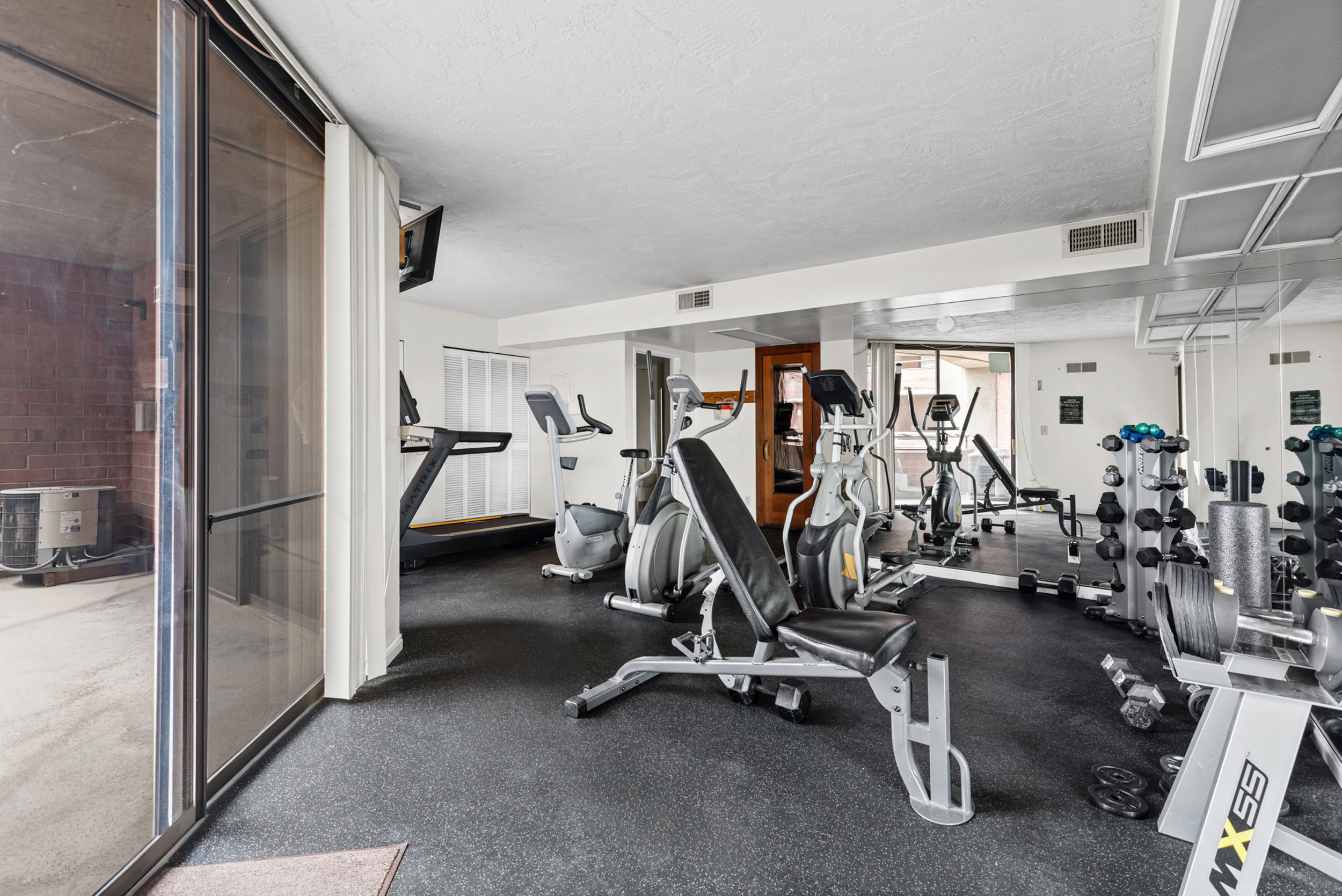 Fitness room featuring resilient rubber flooring, mirrored wall accents, a variety of exercise equipment, and direct access to an outdoor area via sliding glass doors