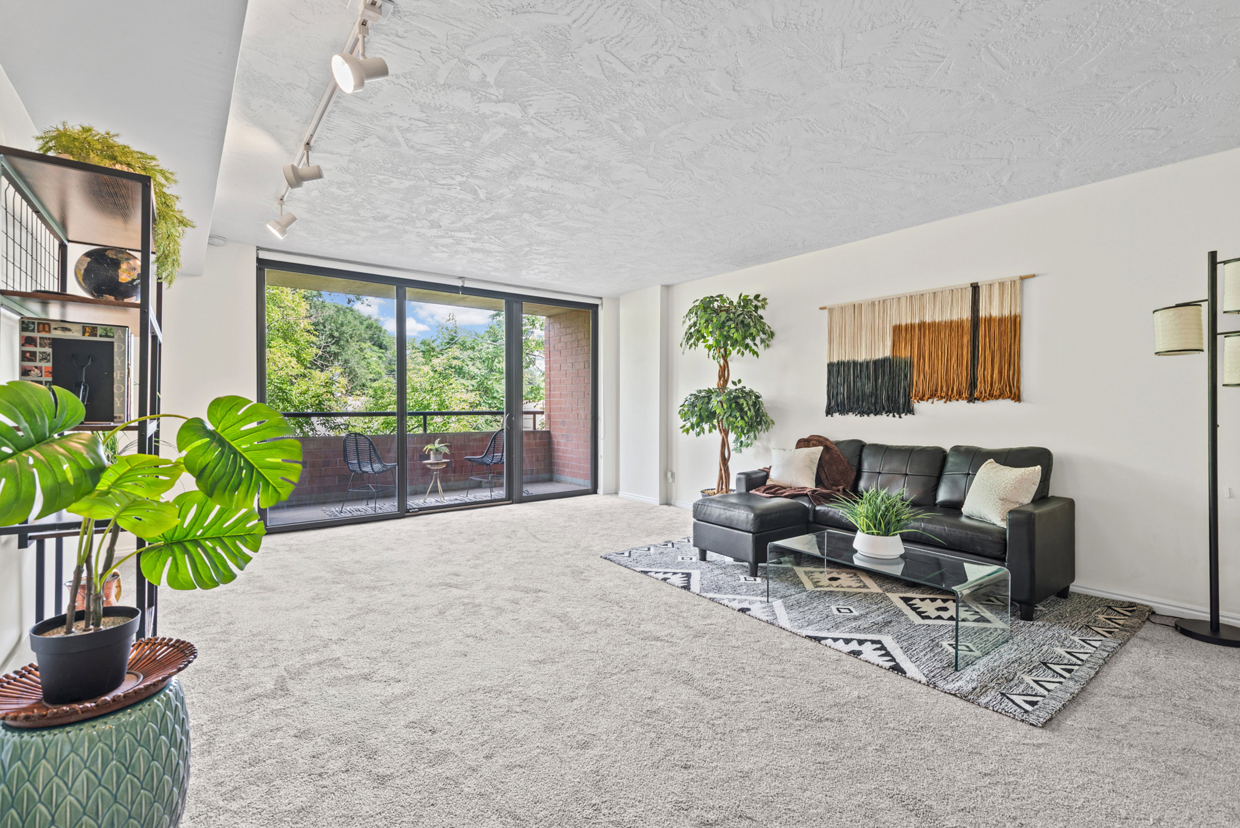 Spacious living area featuring light-colored carpeting and a full-width sliding glass door leading to a private balcony