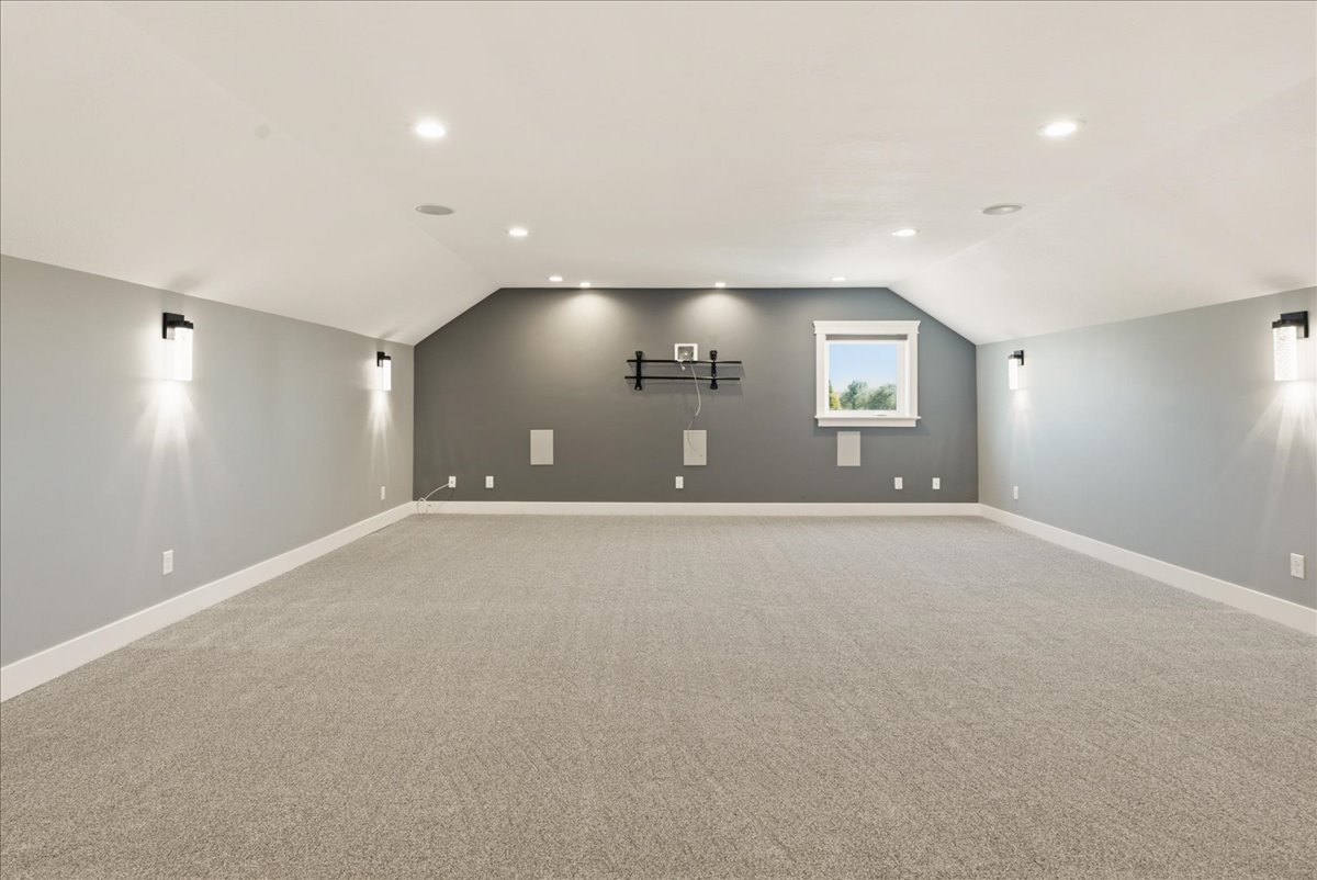 Spacious room featuring sloped ceilings, recessed lighting, wall sconces, built-in speakers, and light-toned carpeting