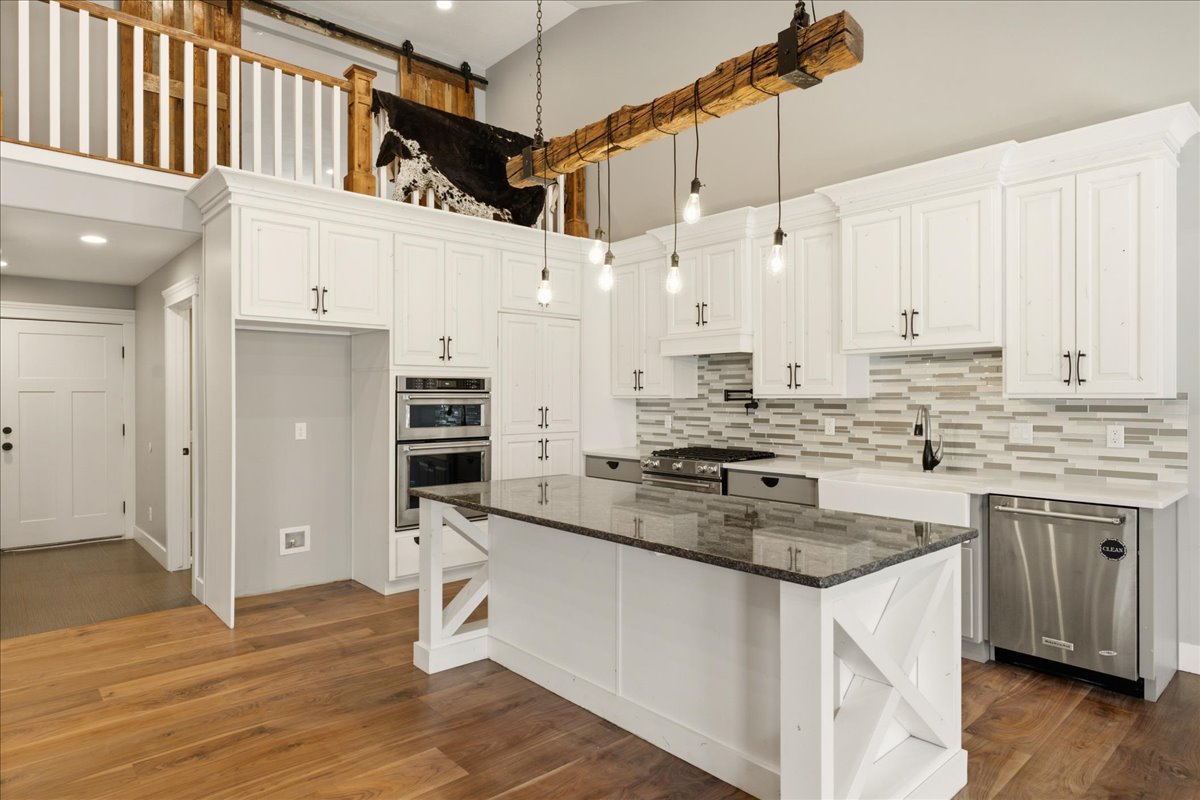 Spacious kitchen featuring white cabinetry, a large kitchen island with a dark countertop, stainless steel appliances, and wood-finish flooring
