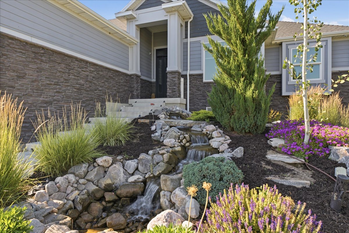 Front exterior featuring a rock-lined water feature, mature landscaping, and an inviting stone and siding facade