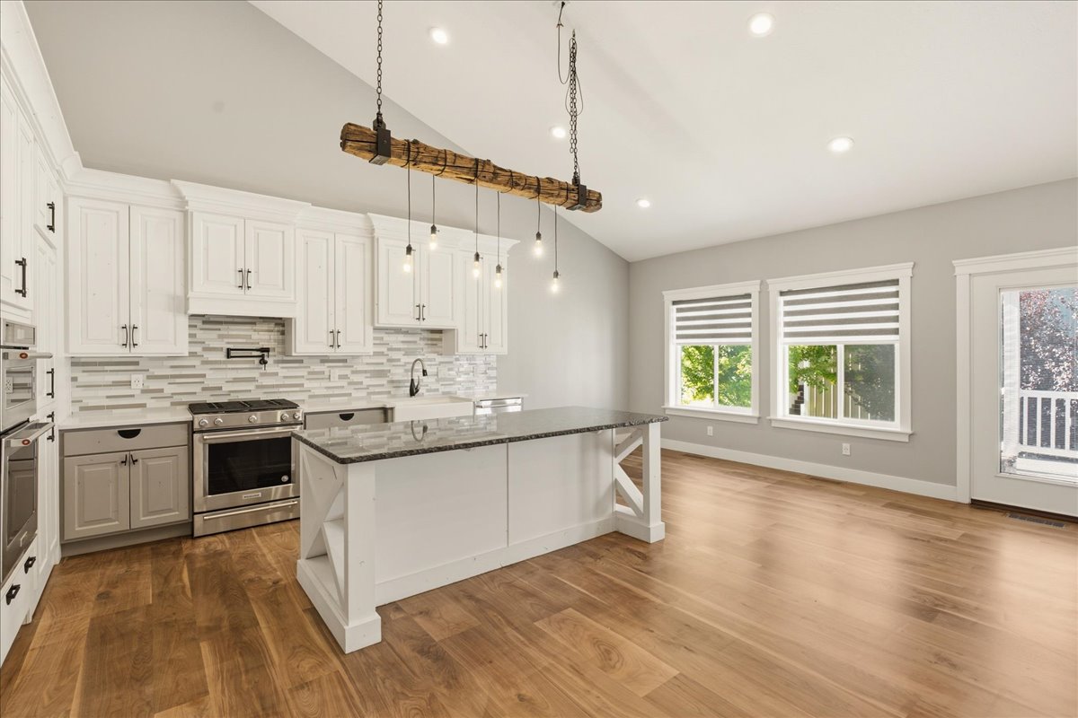 Spacious kitchen featuring white cabinetry, stainless steel appliances, a textured tile backsplash, and a central island with a dark countertop
