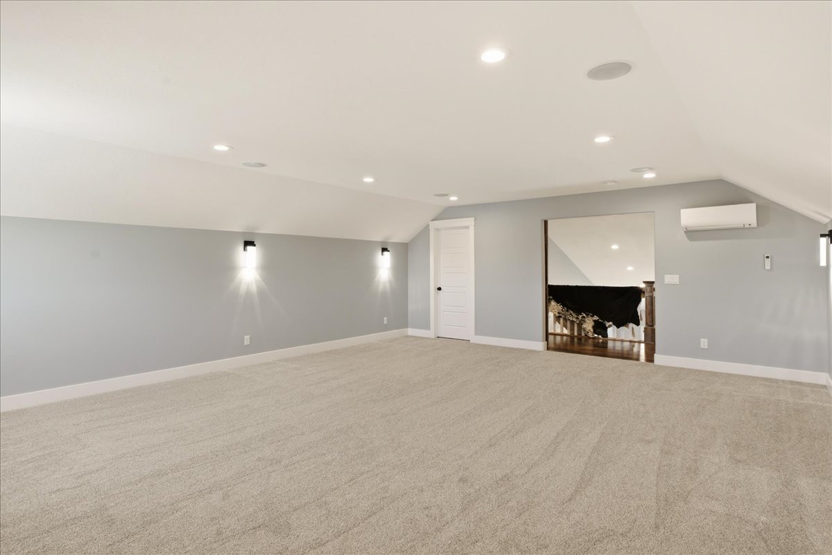 Spacious carpeted room featuring recessed lighting, wall-mounted sconces, a built-in speaker system, and a mini-split climate control unit