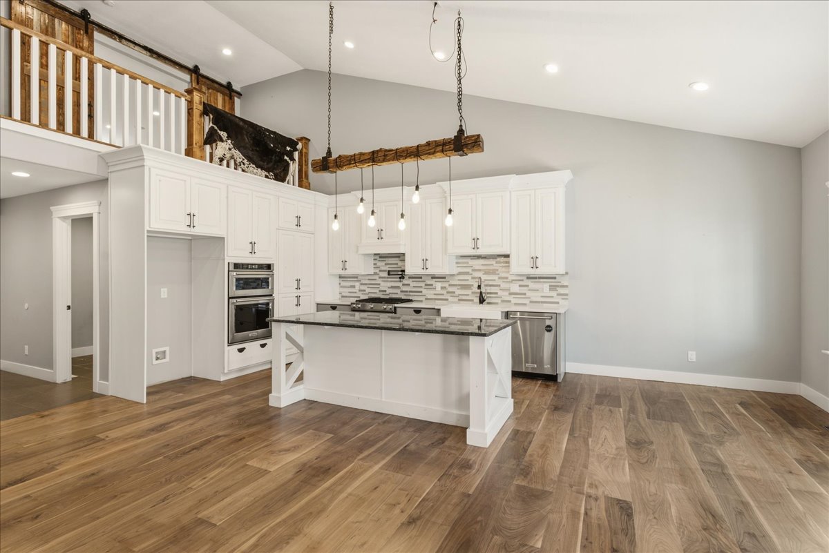 Open-concept kitchen featuring white cabinetry, a central island with a dark countertop, stainless steel appliances, and a unique pendant light fixture