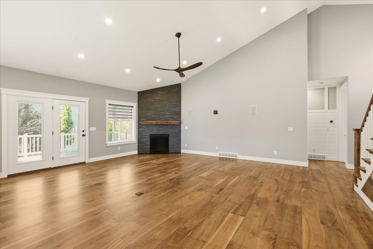 Spacious room featuring wood-finish flooring, a contemporary fireplace with a stone surround and wood mantel, and soaring vaulted ceilings