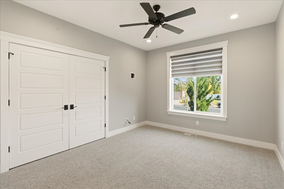 Bright room featuring a large window with horizontal blinds, overhead ceiling fan, recessed lighting, double panel doors with matte black hardware, and gray carpet flooring