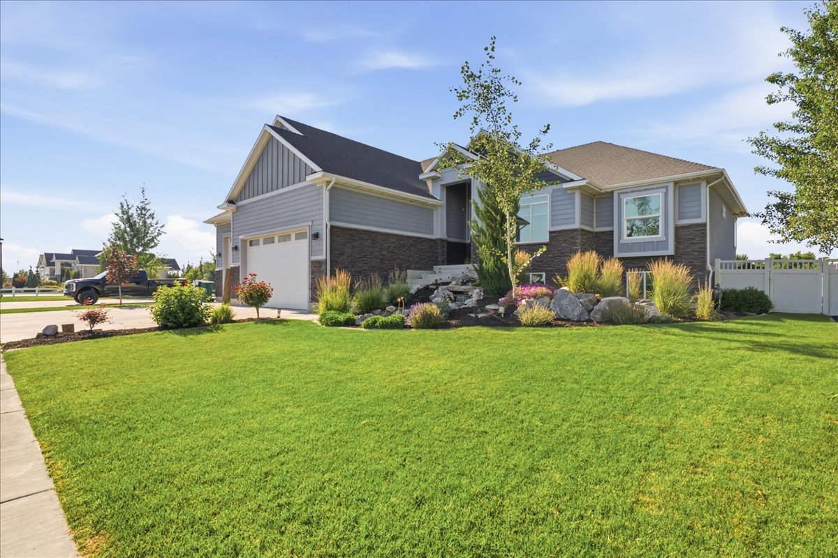 Contemporary exterior featuring mixed material siding, a two-car garage, a well-maintained lawn, and a landscaped rock garden with established plantings and a decorative water feature