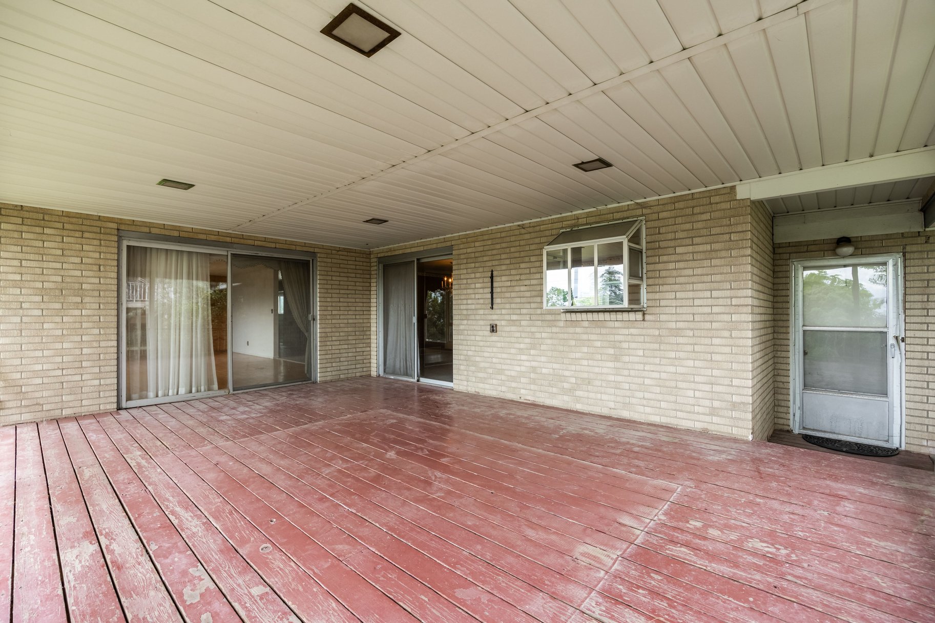 Expansive covered patio featuring a wood-finish floor, light-toned brick exterior, and recessed ceiling lights