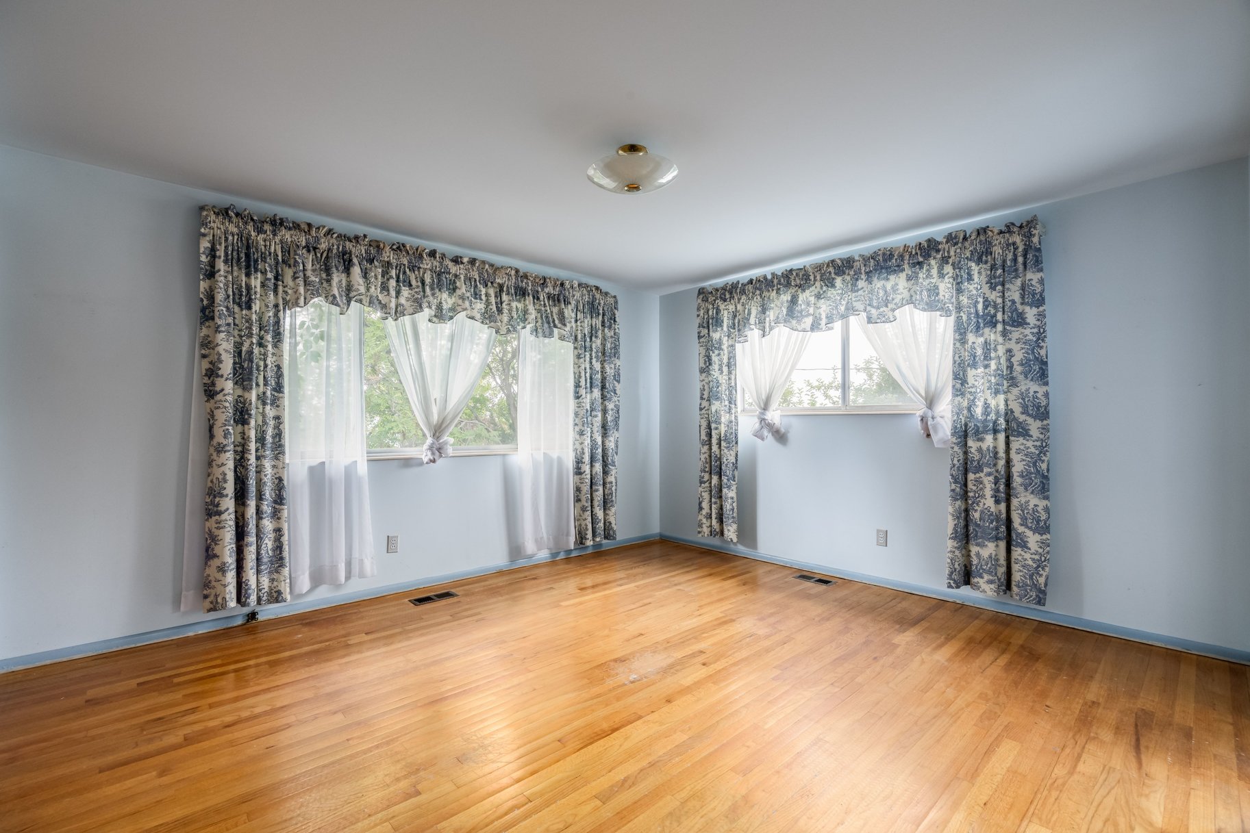 Hardwood flooring throughout featuring two windows with curtain treatments and a ceiling-mounted light fixture