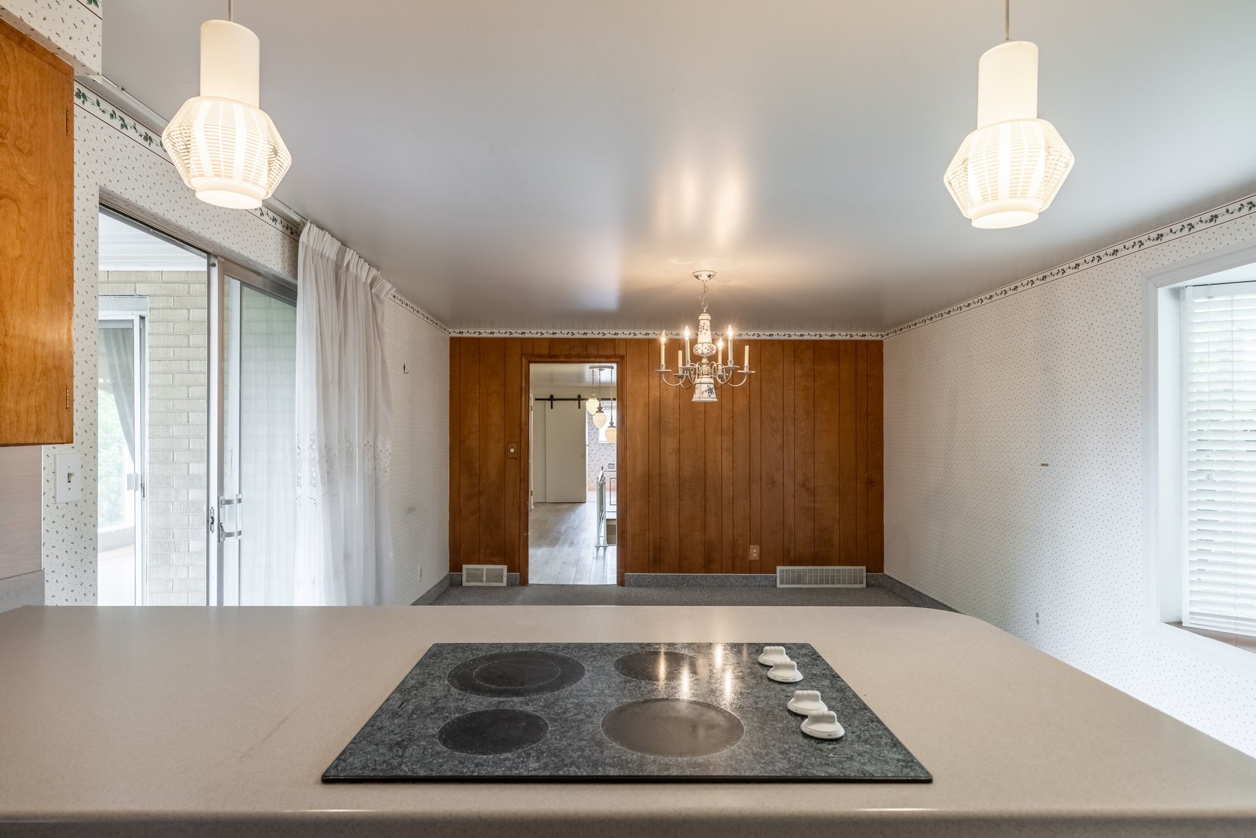 Kitchen island with integrated black cooktop and light-toned countertop, featuring overhead pendant lighting
