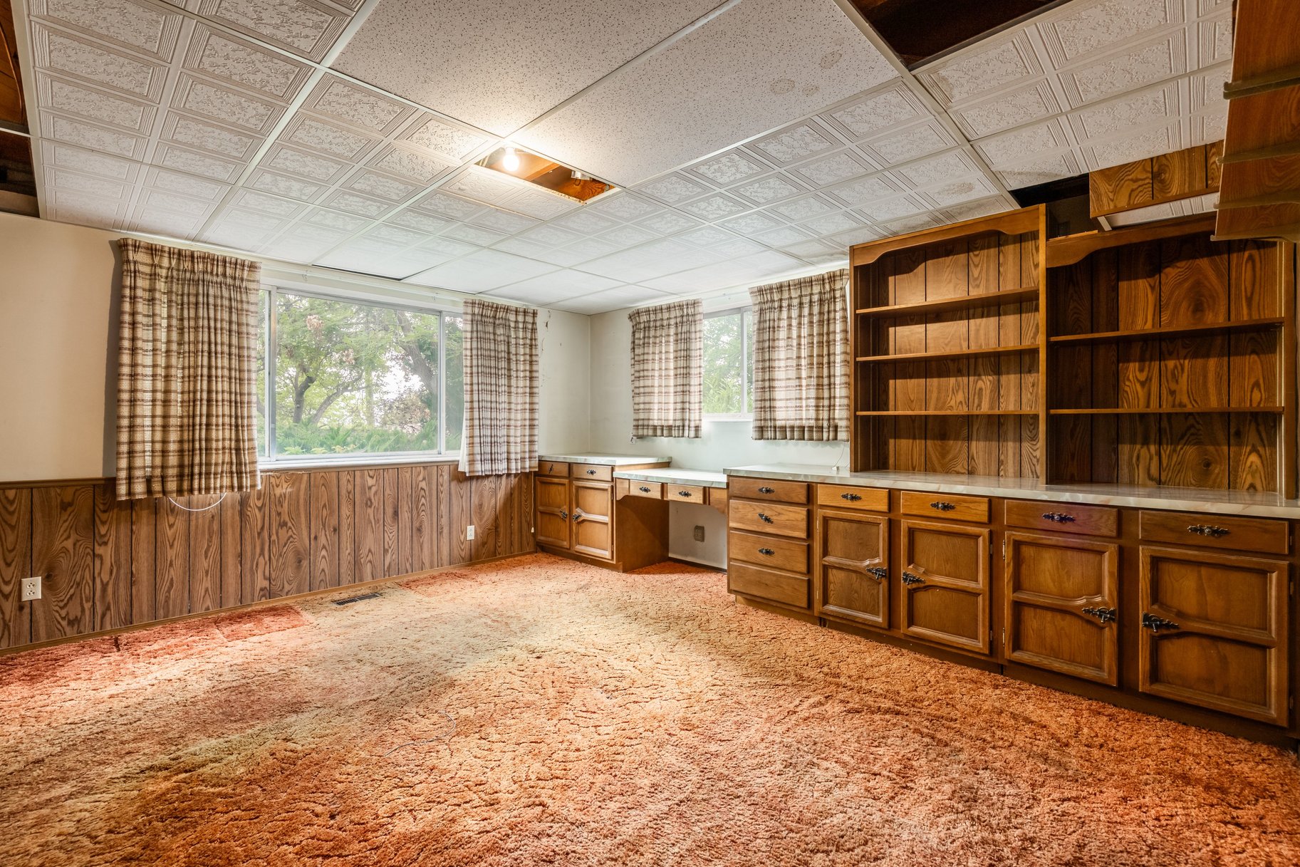 Room featuring wood paneling, drop ceiling, built-in shelving, wood cabinetry with drawers, and a built-in desk area