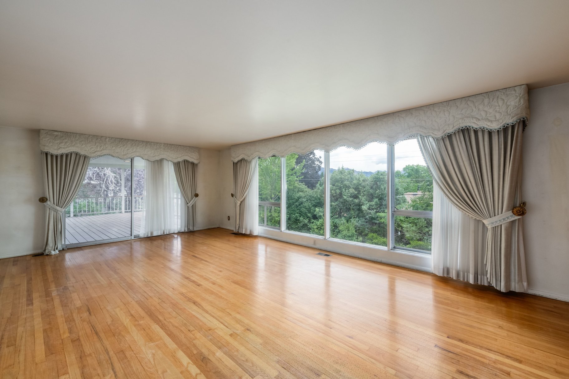Expansive room with wood-finish flooring, large picture windows, and sliding glass doors opening to a deck