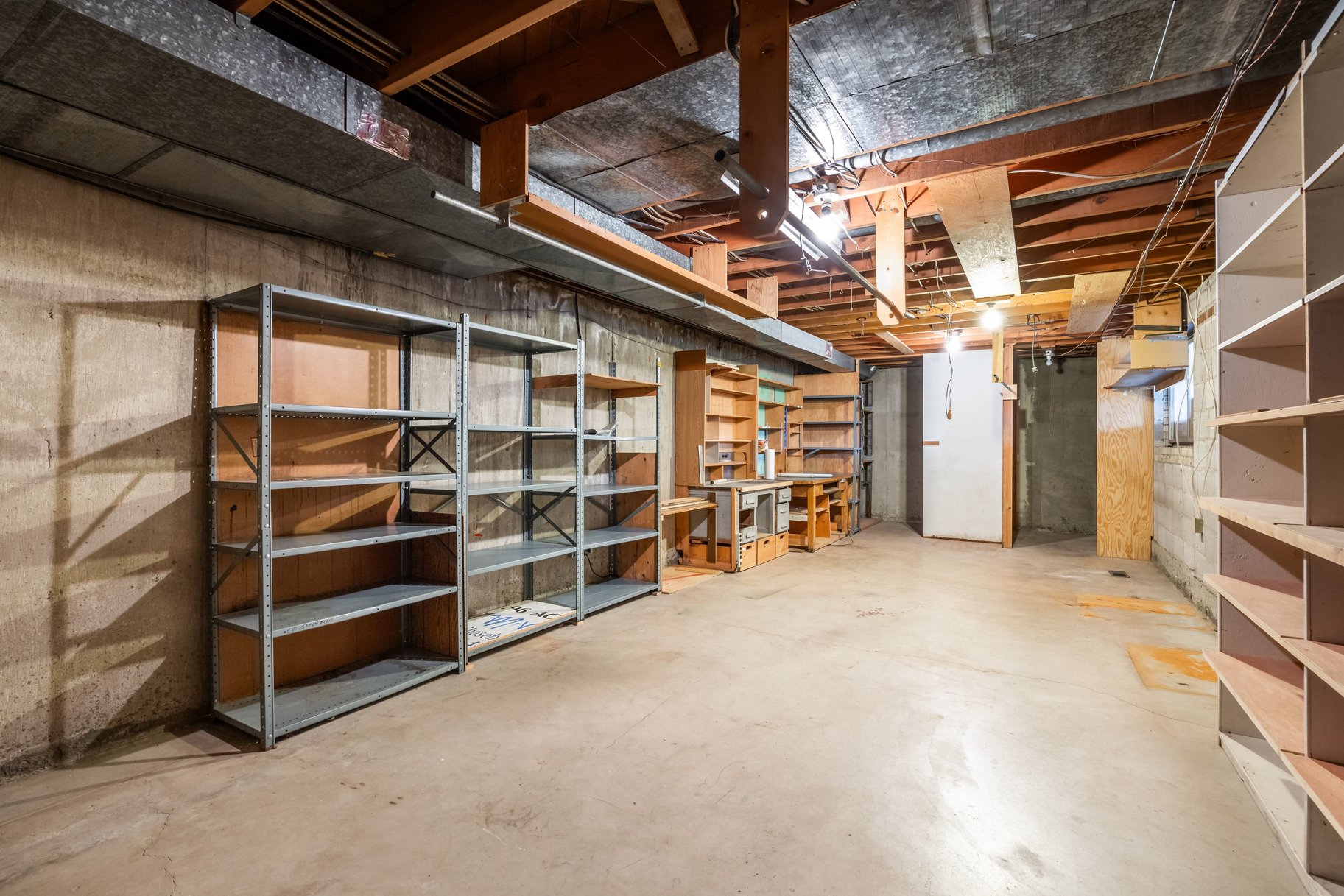 Open basement area featuring exposed ceiling joists, concrete flooring, and ample built-in shelving