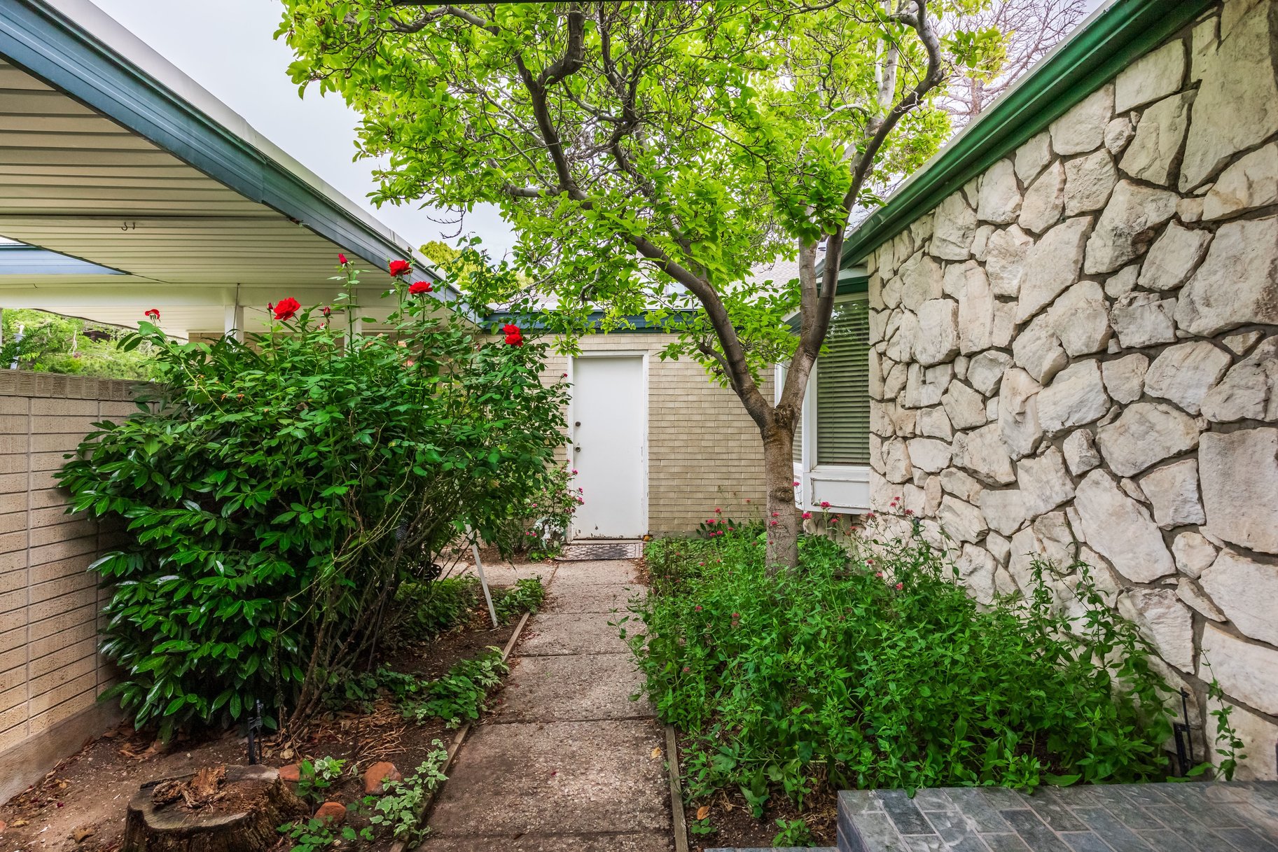 Stone accent wall with a covered walkway and lush landscaping