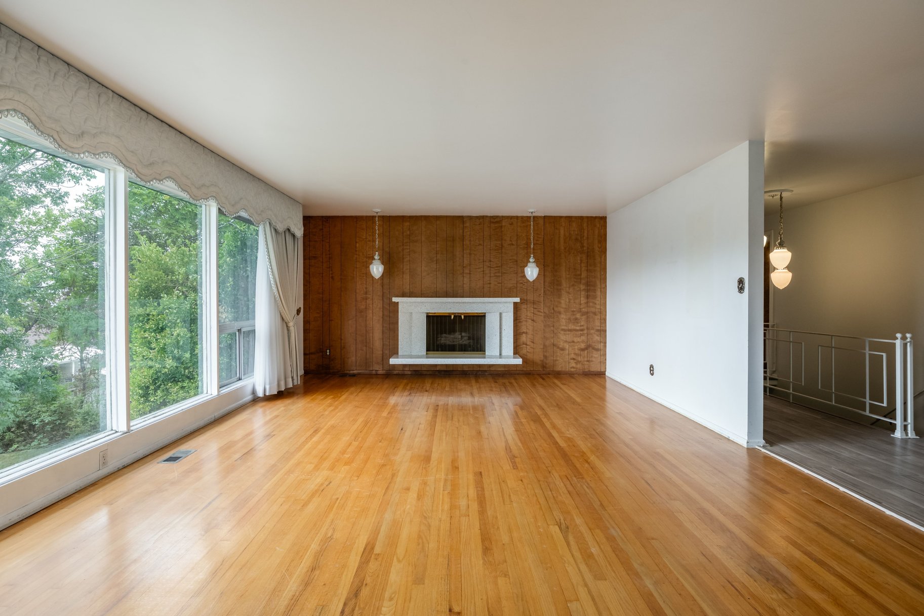Spacious living area featuring large picture windows, wood-finish flooring, a white mantel fireplace, and wood paneling