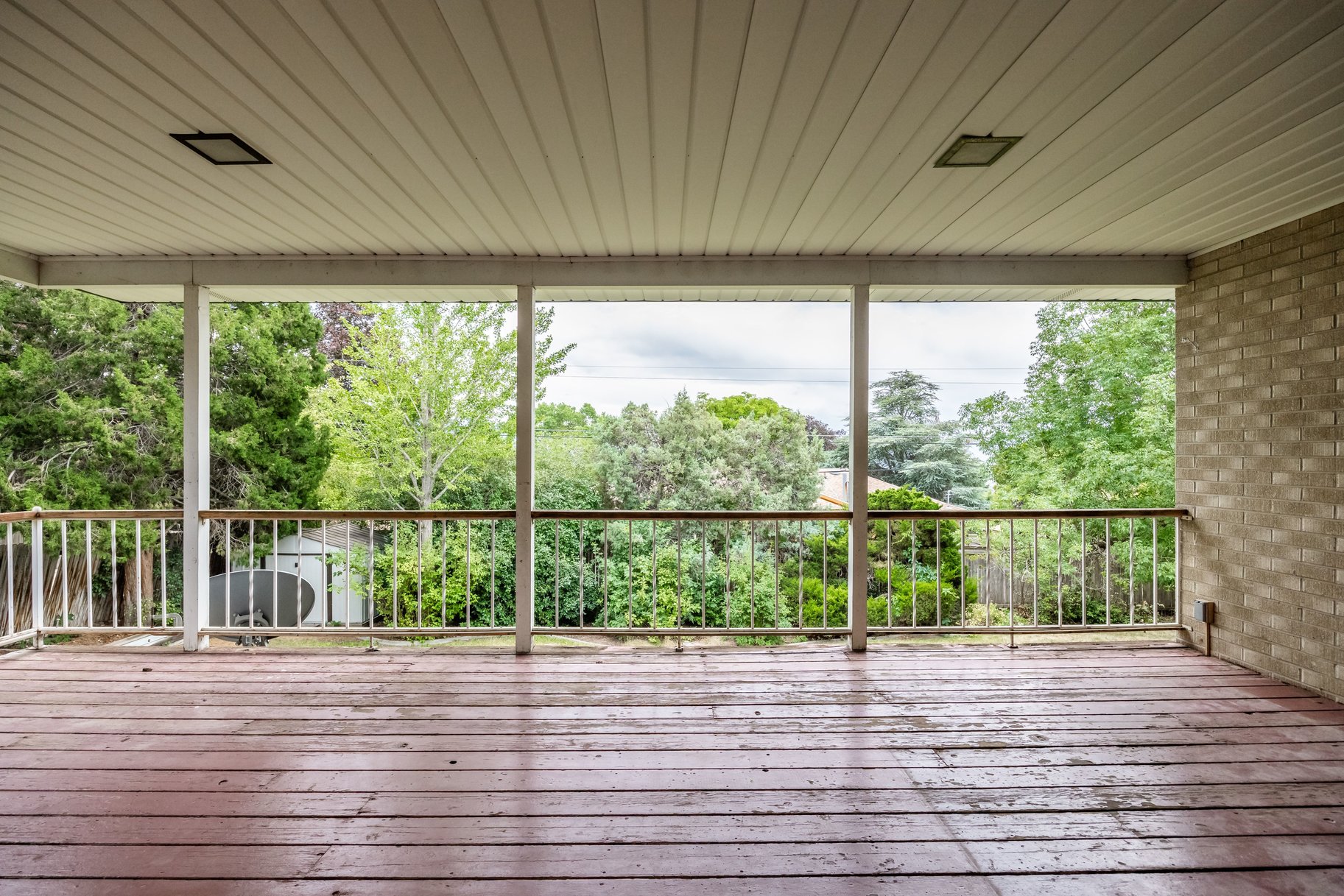 Expansive covered deck featuring wood-finish flooring, white railing, and a brick exterior wall