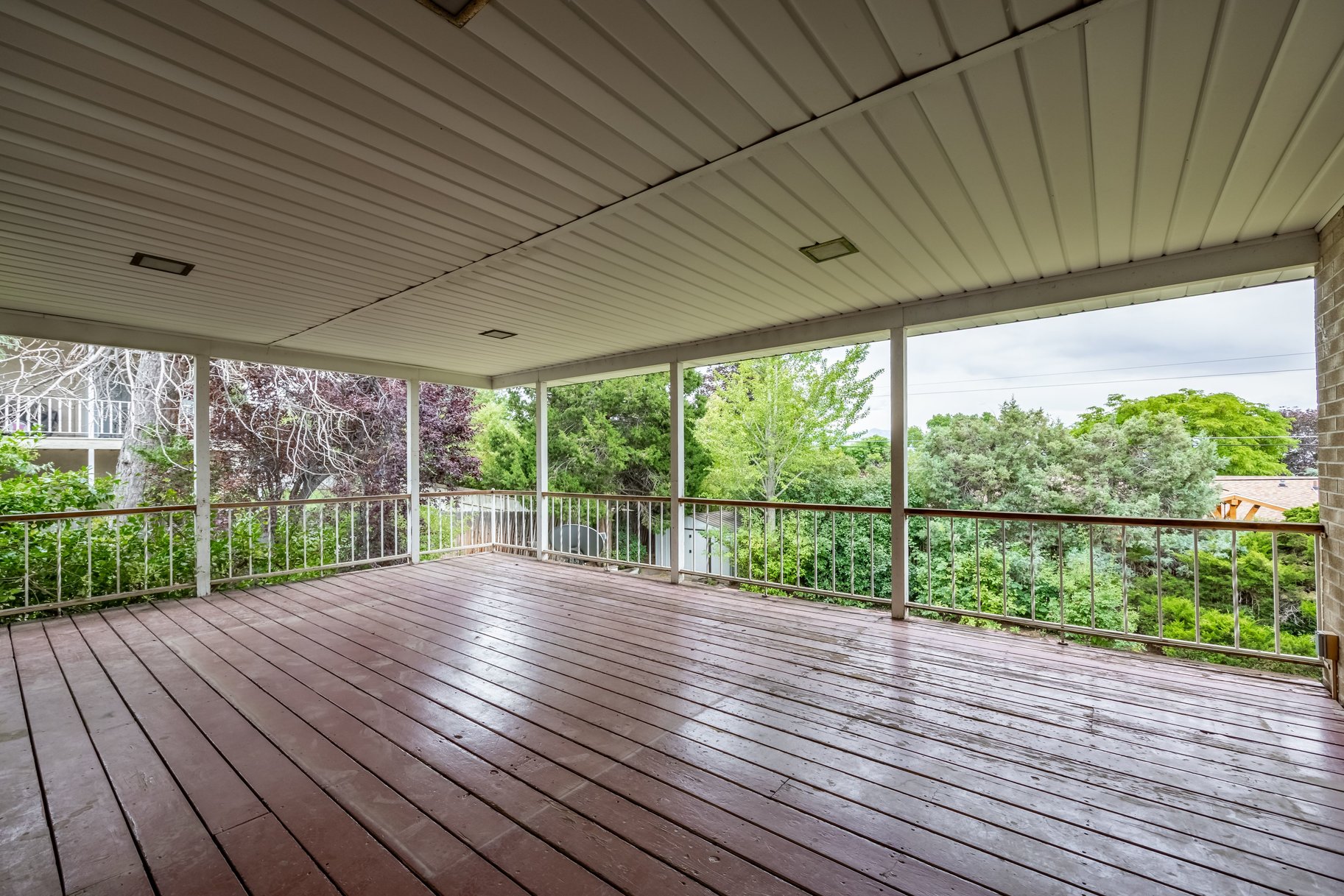 Expansive covered deck featuring wood-finish flooring, white railing with a wood-finish top rail, and recessed lighting