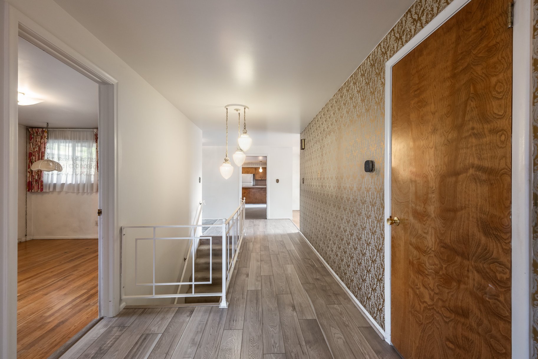Hallway featuring wood-finish flooring, a contemporary multi-light pendant fixture, white painted walls, and an accent wall with patterned wallpaper