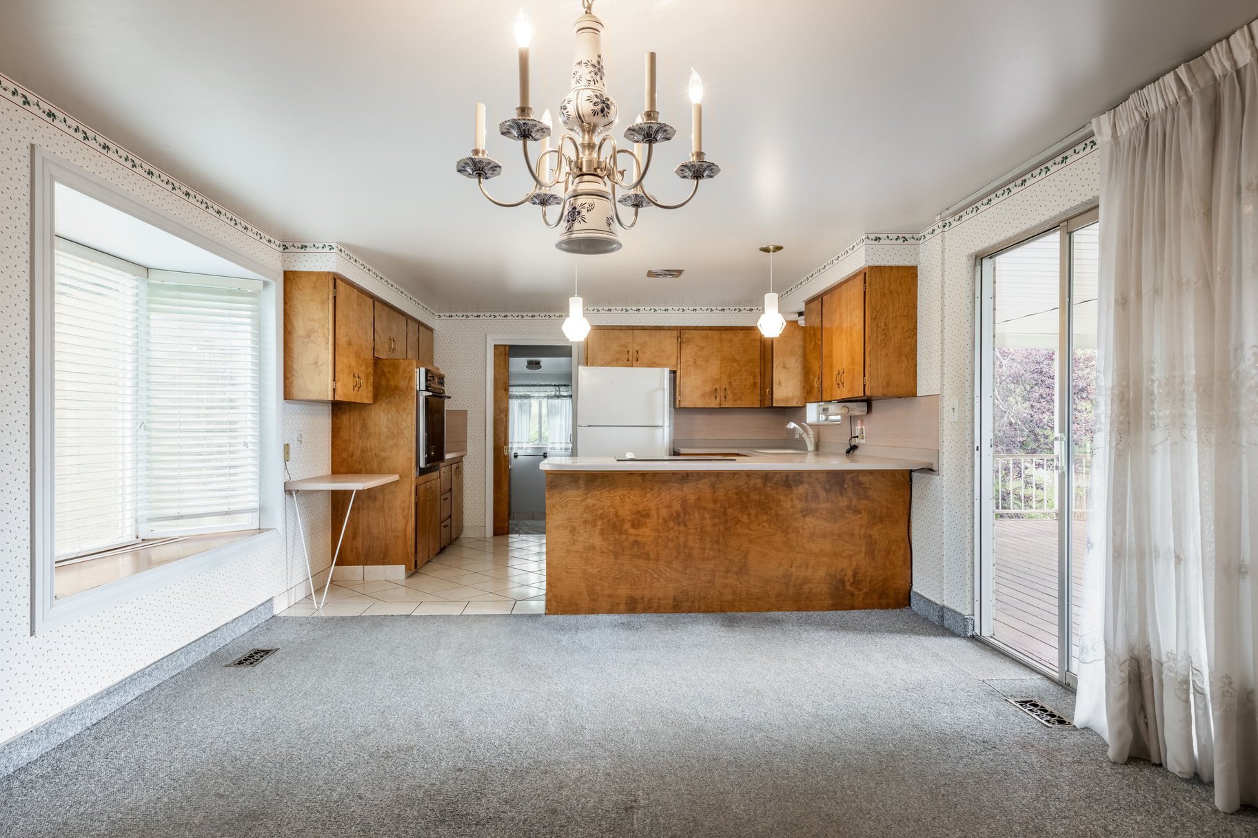 Kitchen and living area featuring a bay window with blinds, wood-finish cabinetry, a built-in oven, and a sliding glass door leading to an outdoor deck