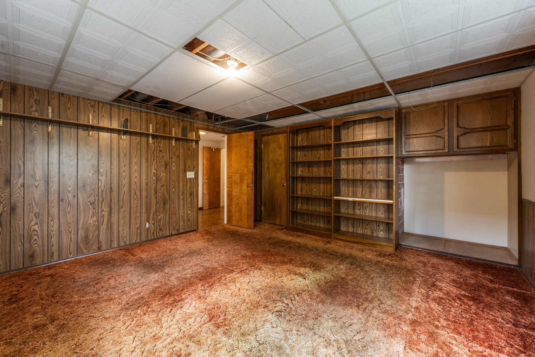 Room featuring wood paneling, extensive built-in shelving, integrated cabinetry, and a drop ceiling