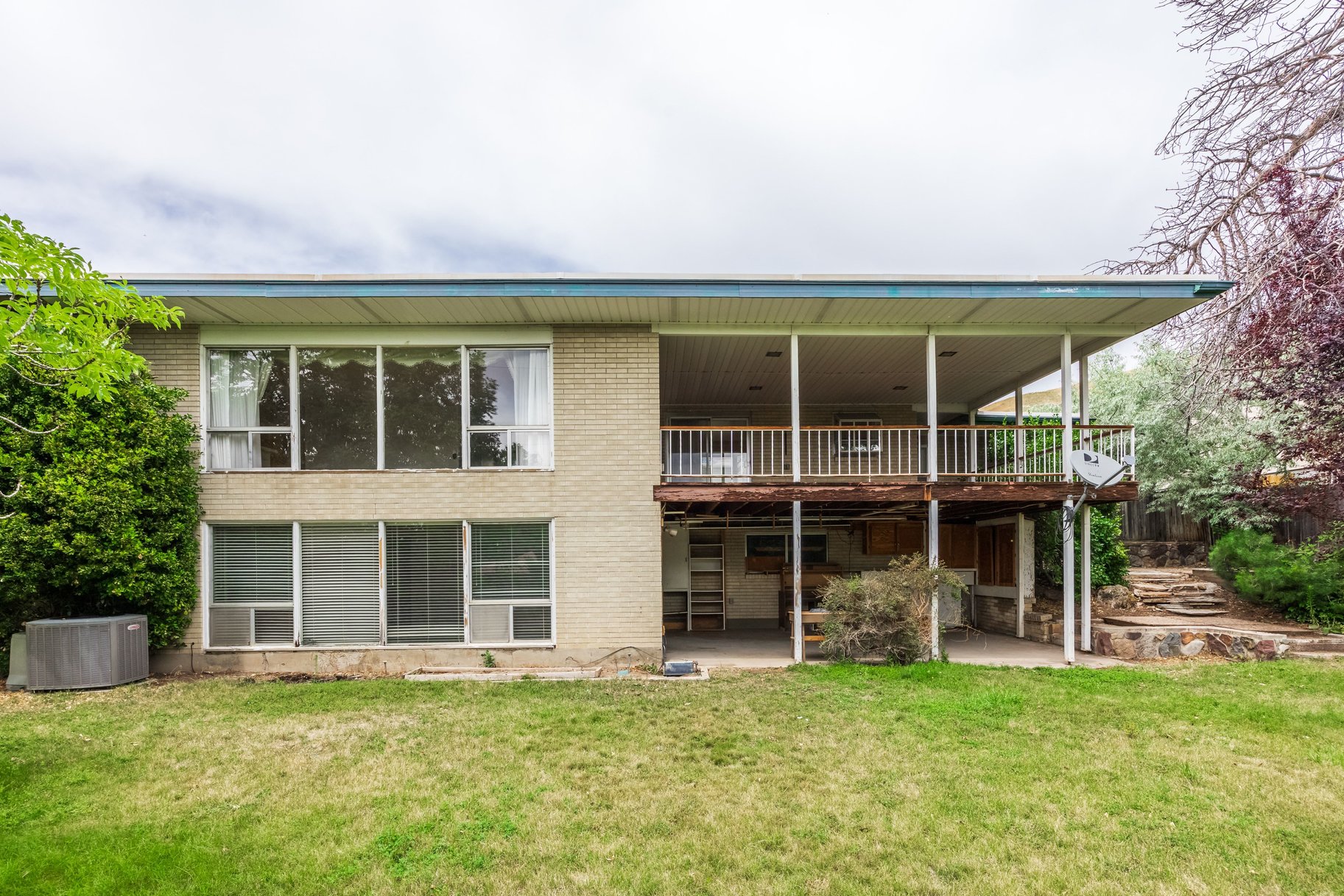 Rear exterior featuring a covered upper deck with wood railing, a covered ground-level patio, and a tiered stone pathway