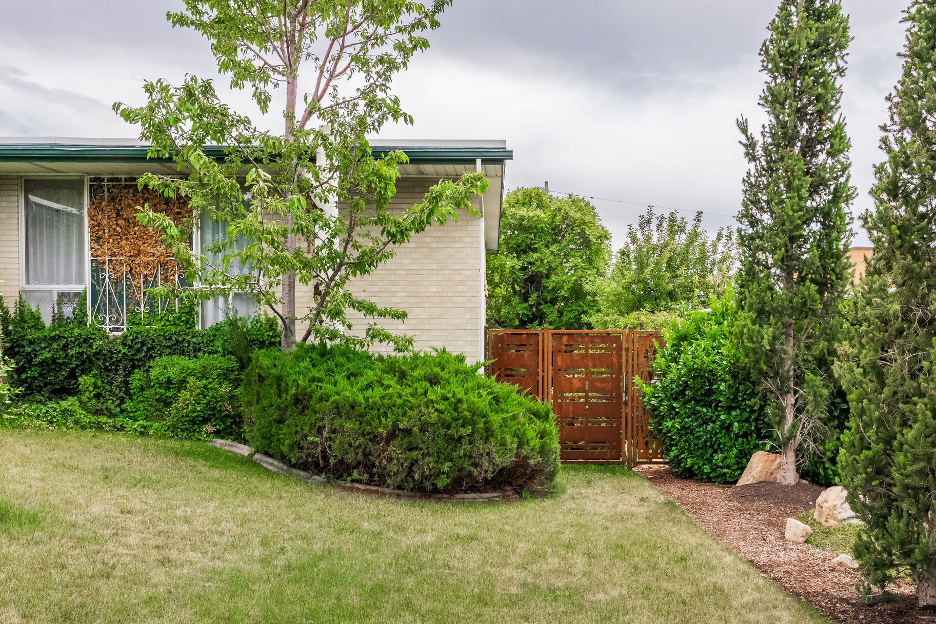 Front exterior featuring light brick masonry, a green fascia, established landscaping, and a decorative privacy fence