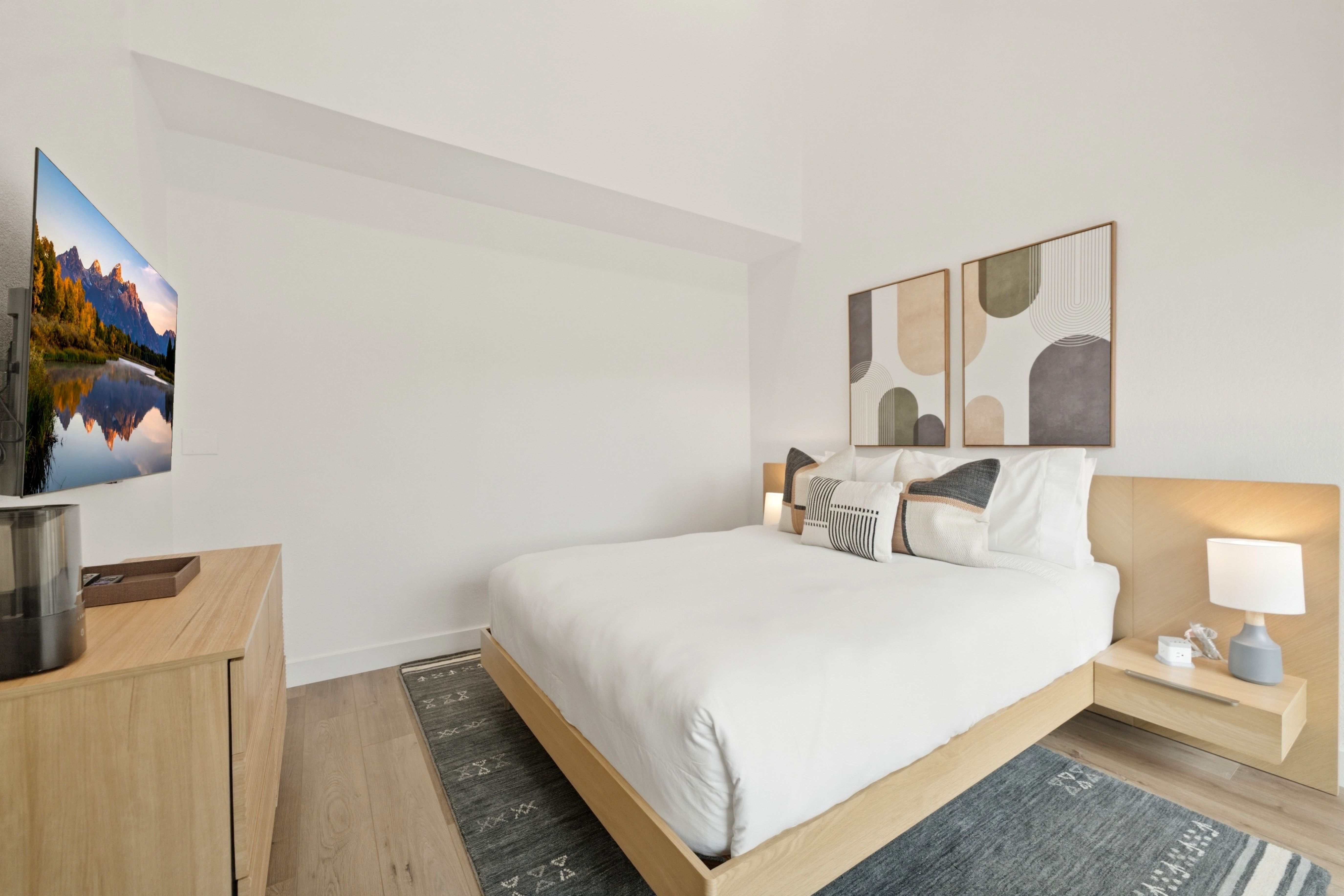 Bright bedroom featuring light wood-finish flooring, white walls, and a wall-mounted television