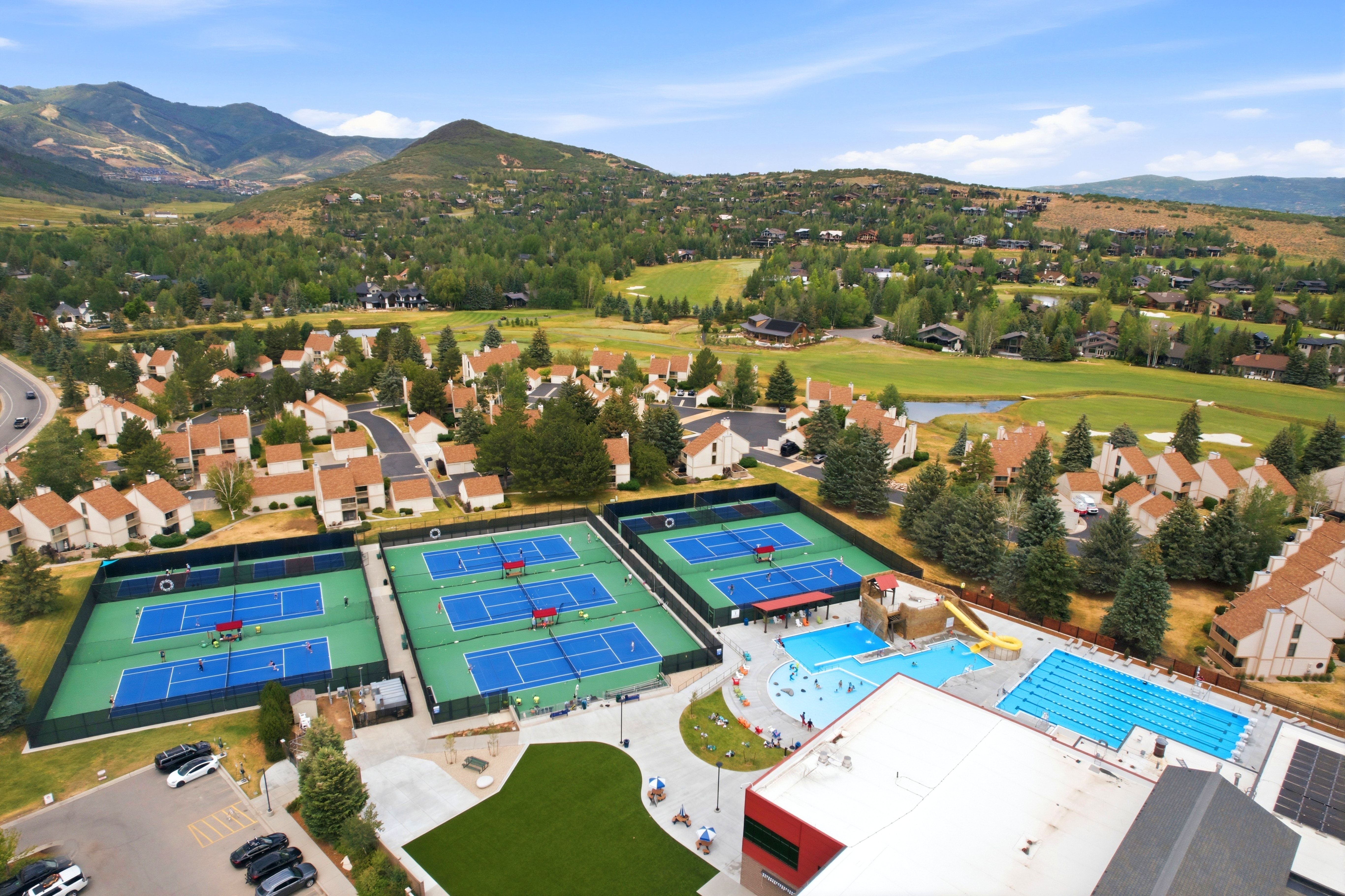 Aerial perspective showcasing multiple tennis courts, an outdoor pool area with a separate lap pool, and surrounding residential structures