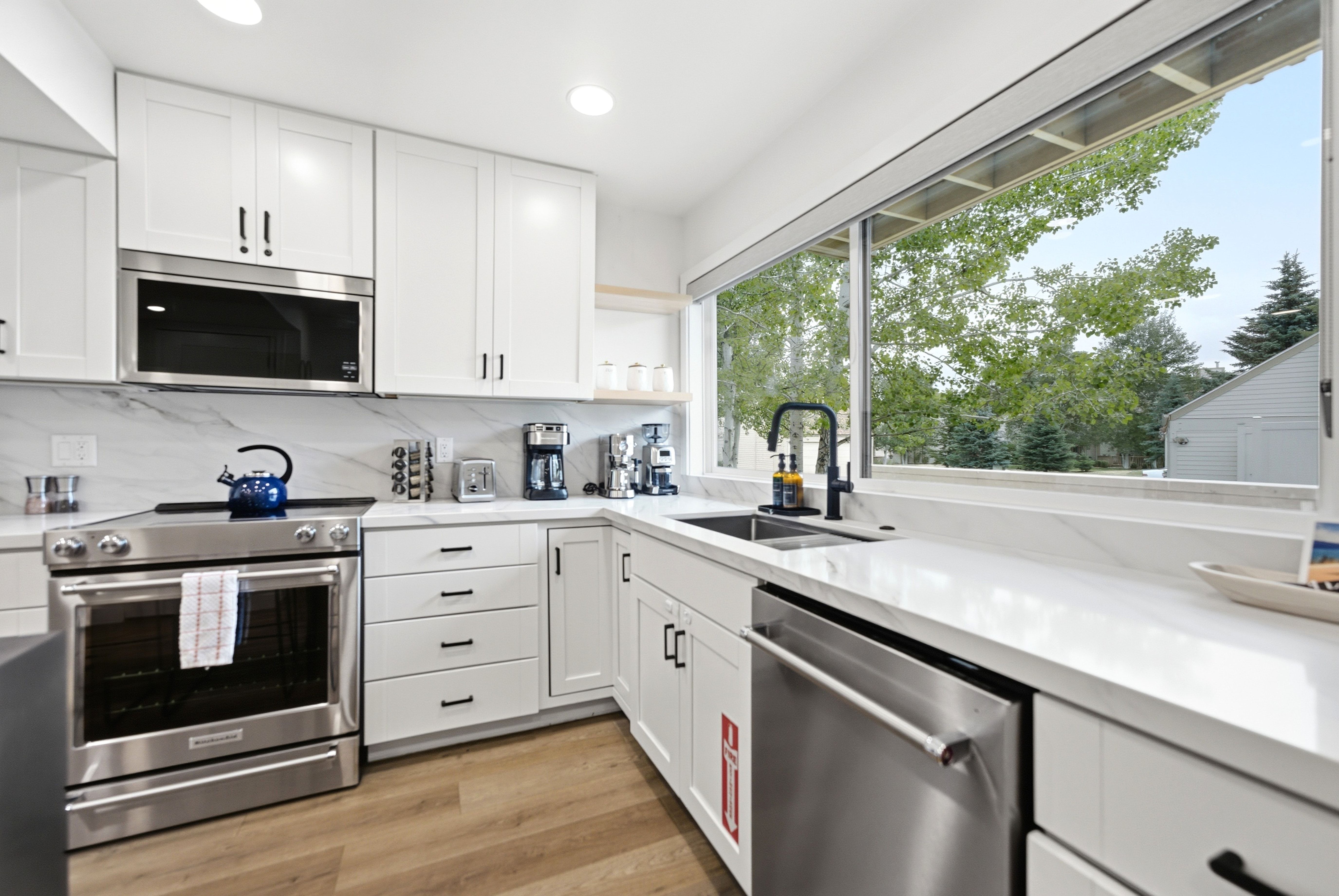 Modern kitchen featuring white cabinetry, stainless steel appliances, a white stone countertop, and wood-finish flooring