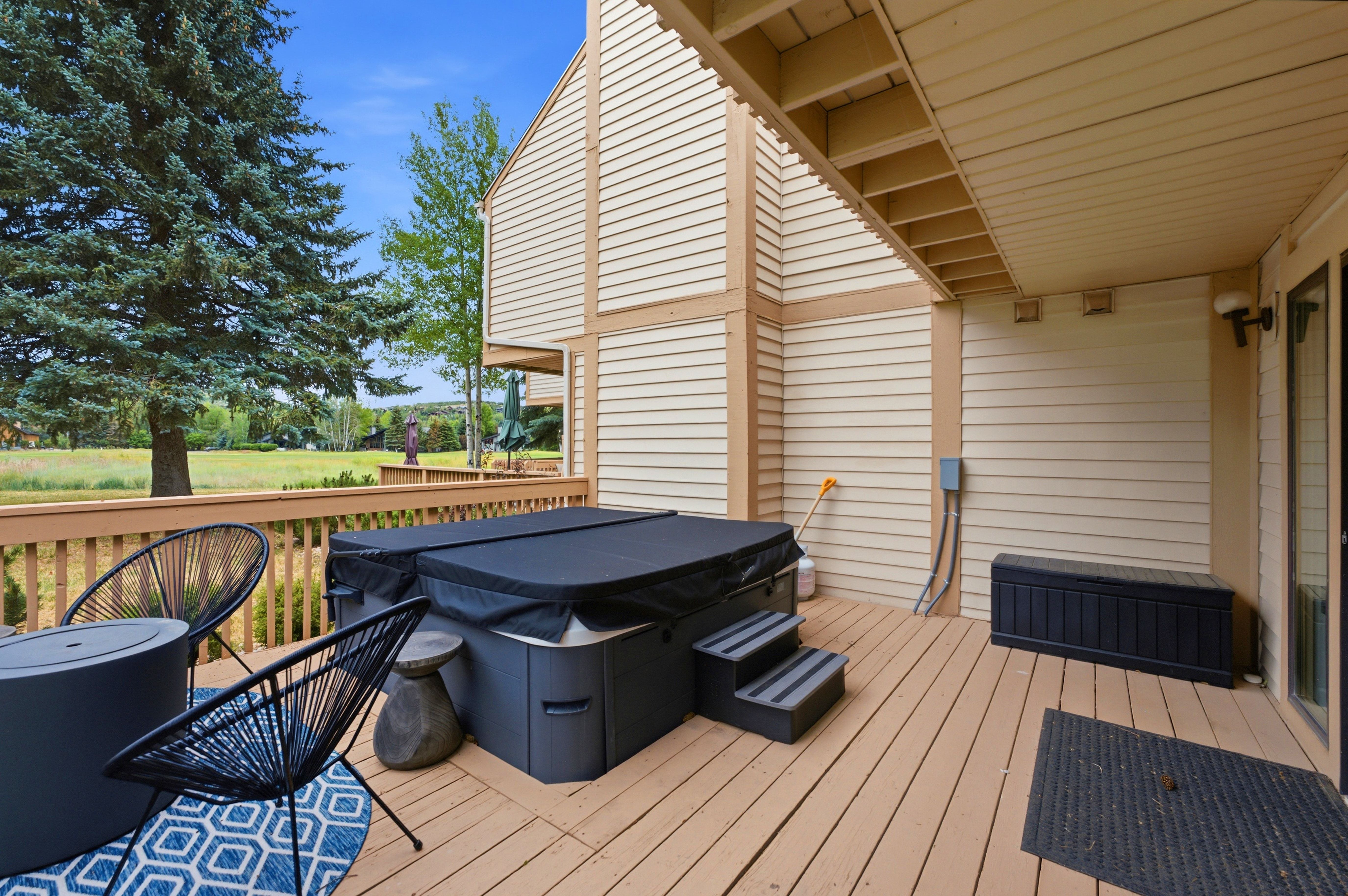 Spacious outdoor deck featuring natural wood-finish flooring, a built-in spa, and direct access to an expansive green space