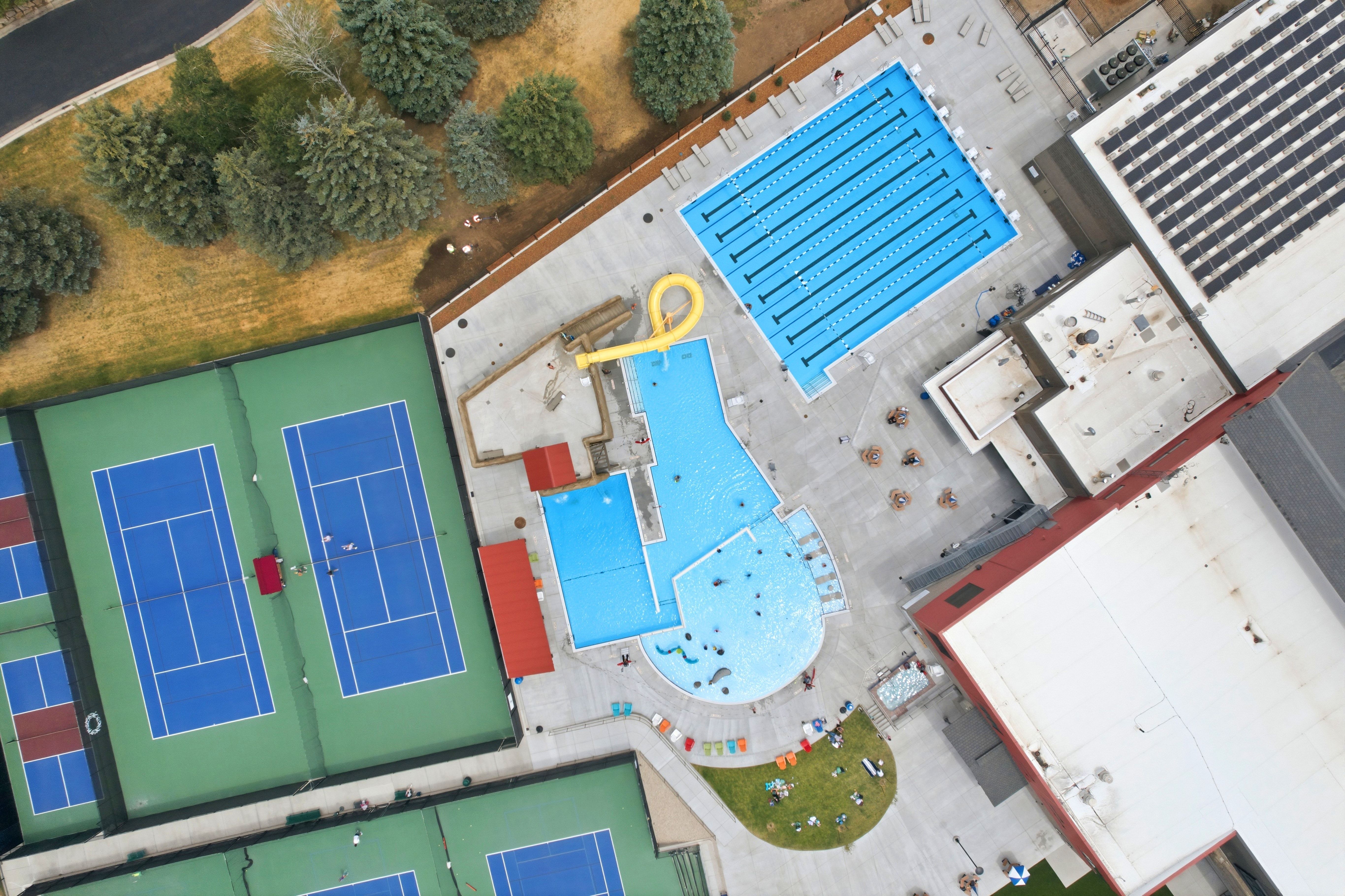 Aquatic center featuring a multi-lane lap pool, a curved leisure pool with a water slide, and ample concrete decking